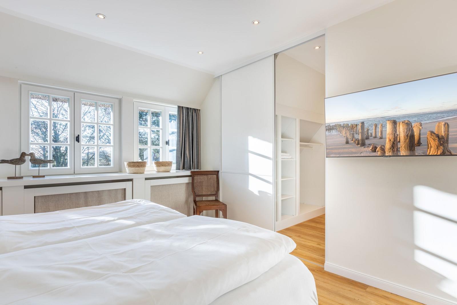 Schlafzimmer mit Bett, Fenster, Kleiderschrank und Wandbild.