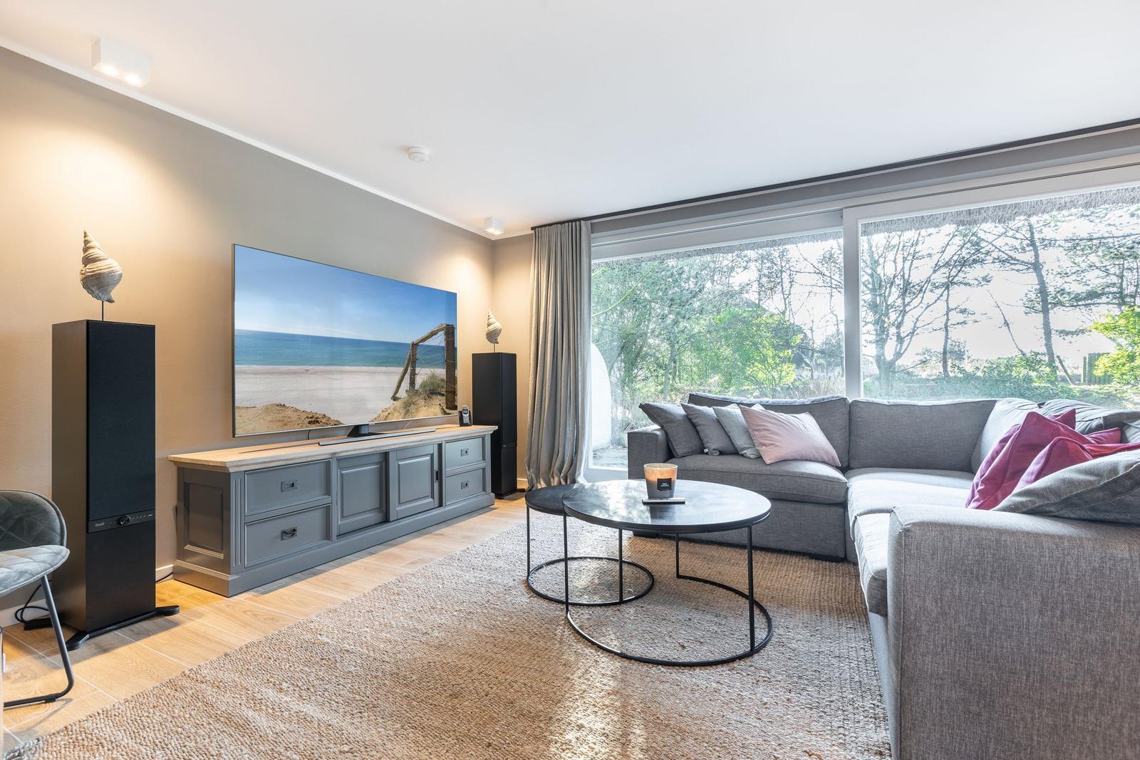 Ein Wohnzimmer mit grauem Sofa, runden Tischen und großem Fenster.