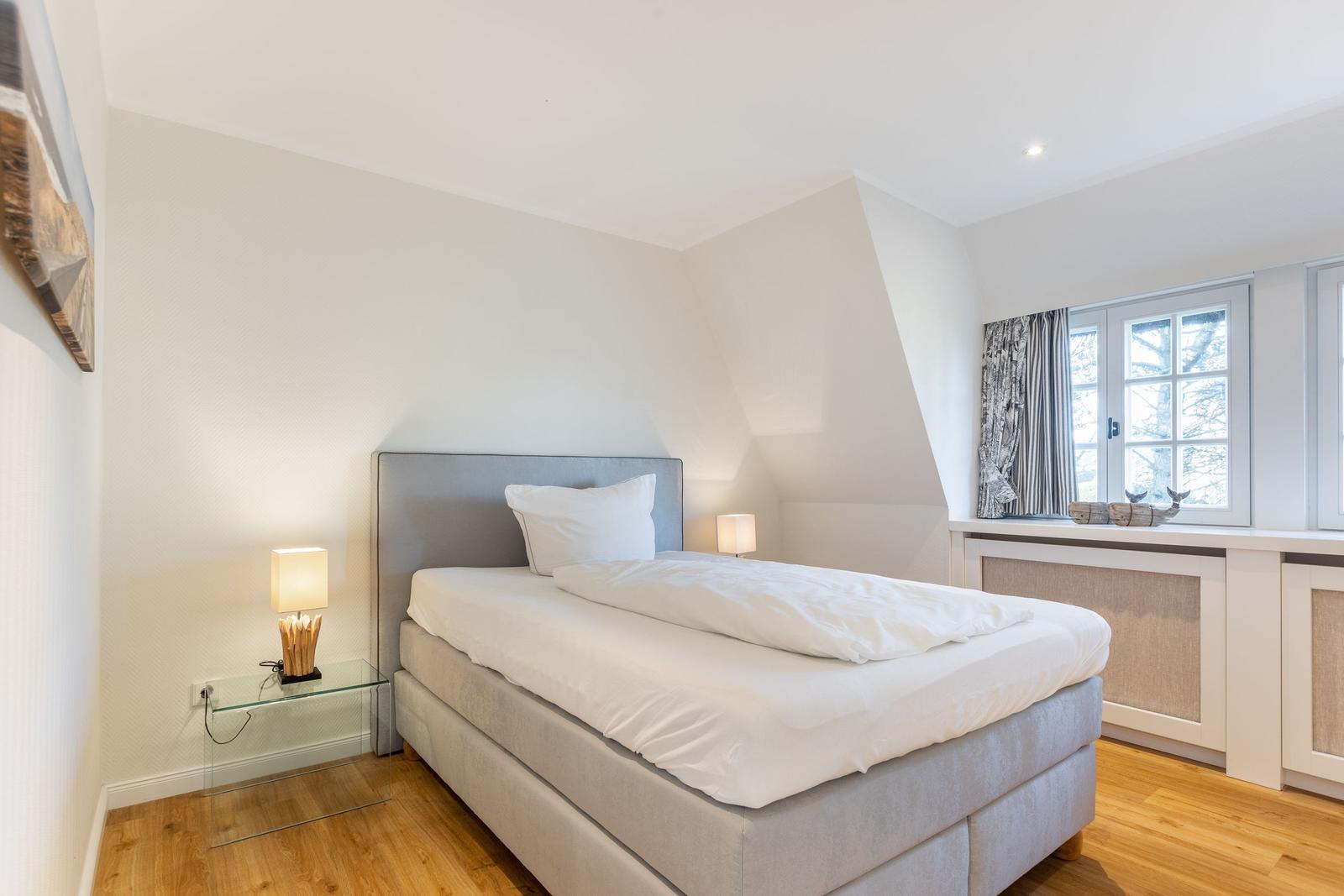 Schlafzimmer mit Doppelbett, Nachttisch und Fenster mit Vorhängen.