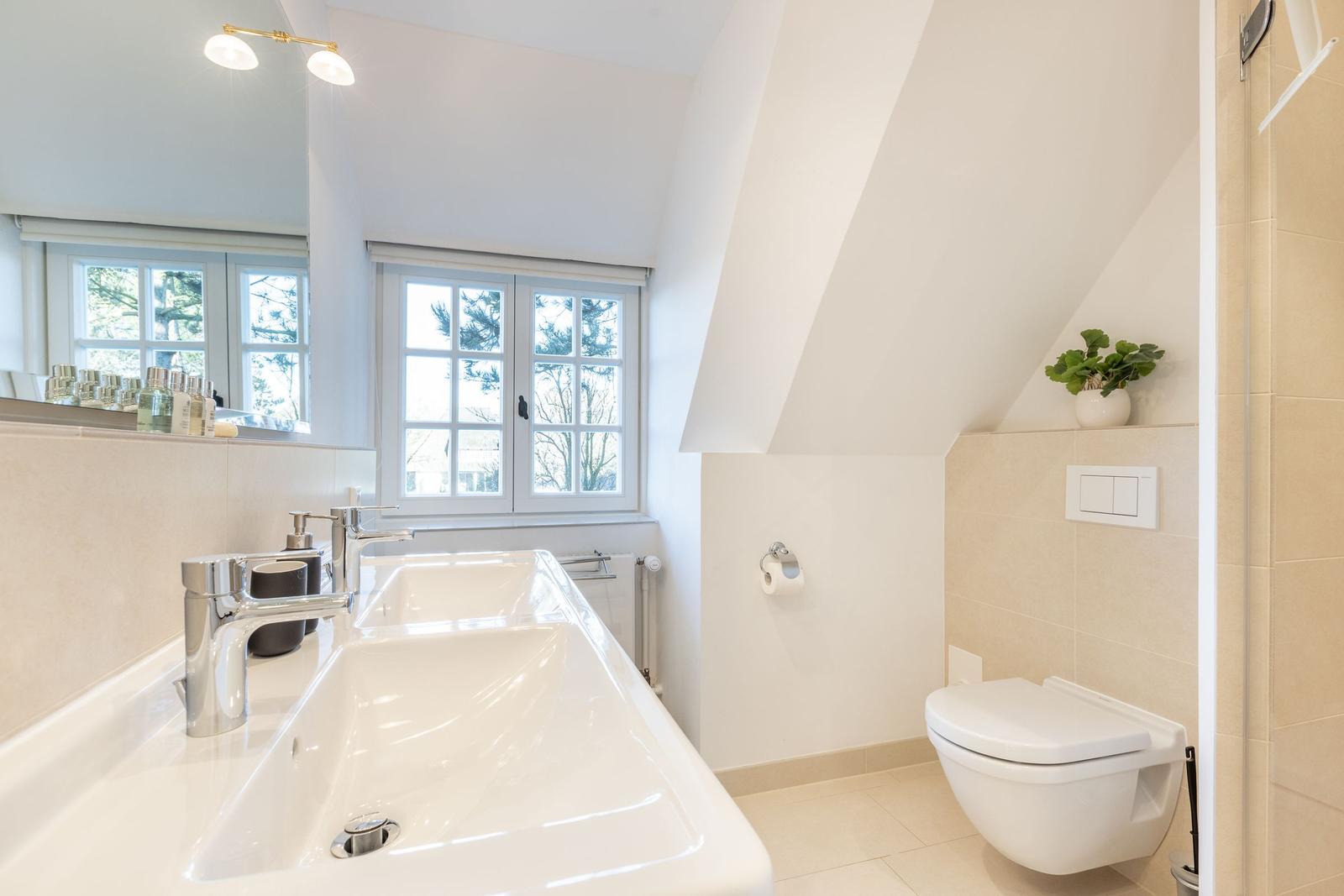 Badezimmer mit Doppelwaschbecken, Toilette und Fenster mit Blick auf Bäume.