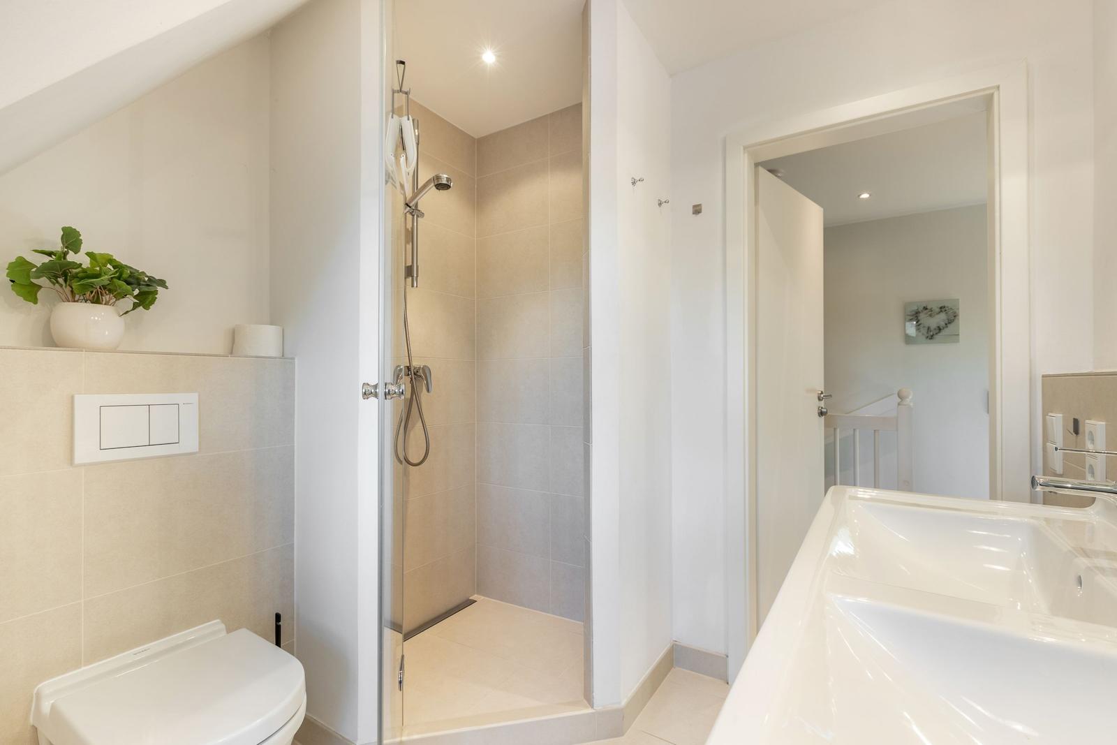 Bad mit Dusche, Waschbecken und Toilette. Pflanze auf der Wand.