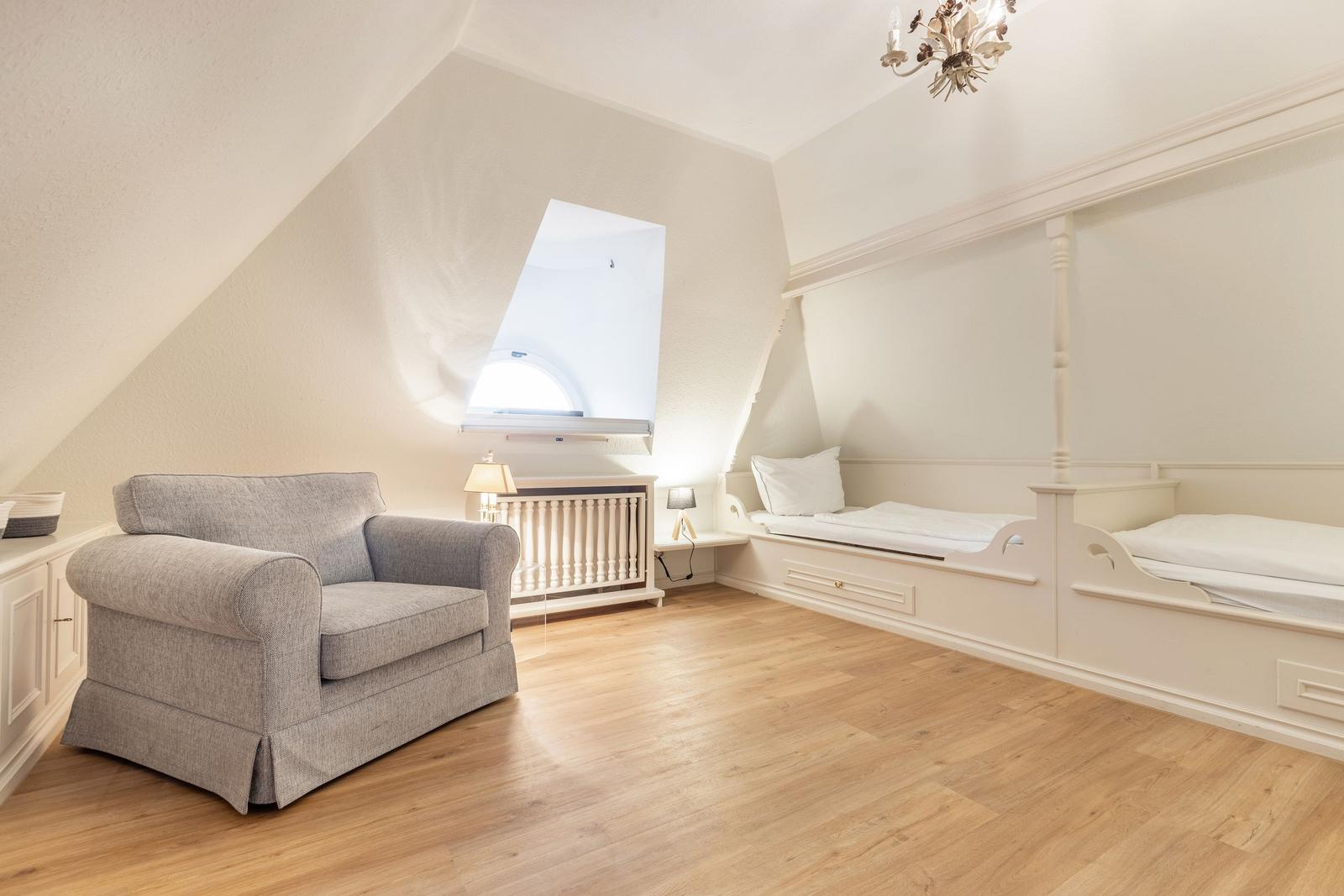 Schlafzimmer mit zwei Einzelbetten und Sessel unter schrägen Dachschrägen.