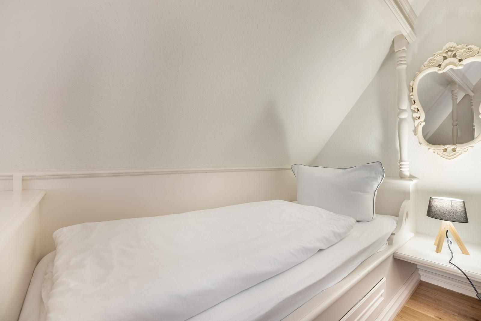 Ein Schlafzimmer mit weißem Bett, Spiegel und Lampe an der Wand.