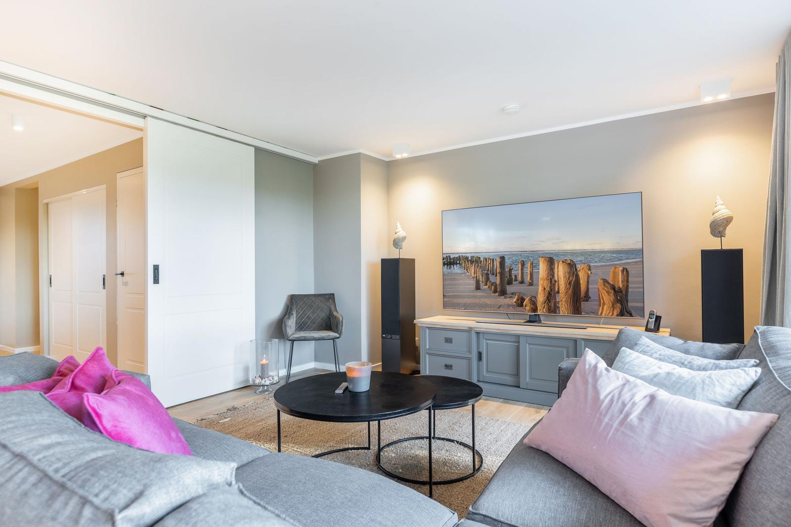 Wohnzimmer mit Sofa, TV und Schwebetüren. Wandbild zeigt Strand.