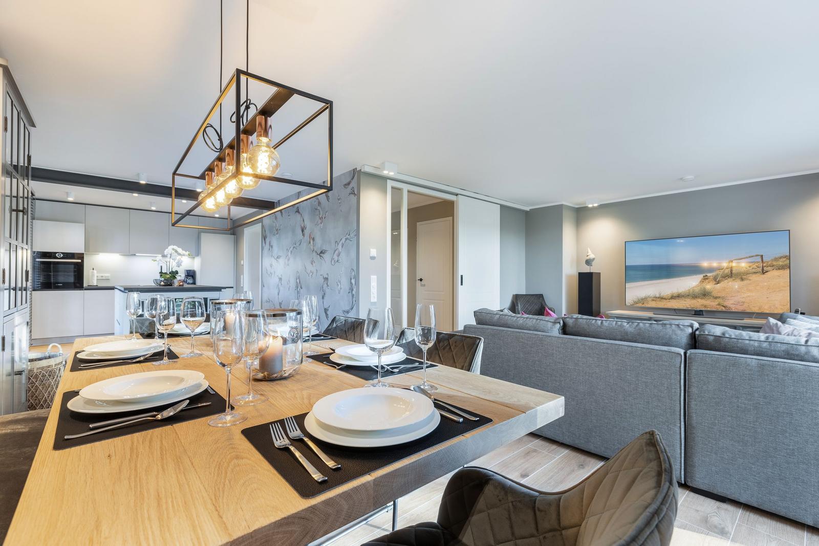 Essbereich mit Tisch und Stühlen, Küche und Wohnzimmer mit Sofa und Fernseher