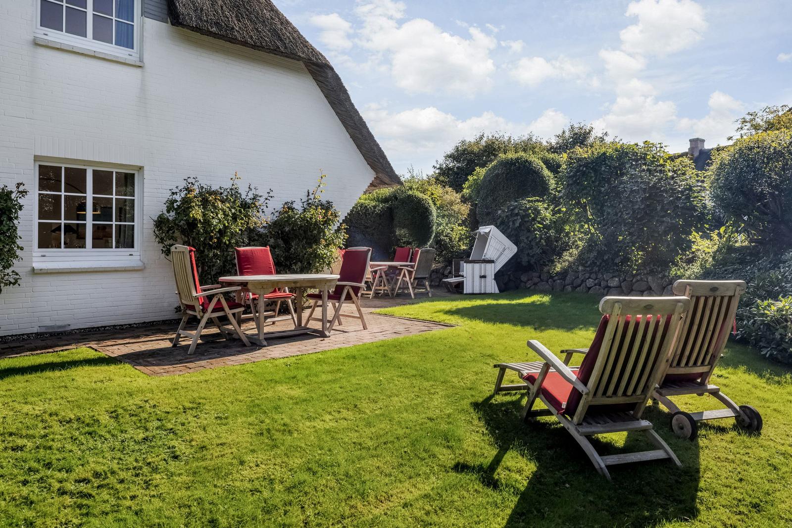 Backyard with lawn, patio, and garden chairs in front of a white house with thatched roof.