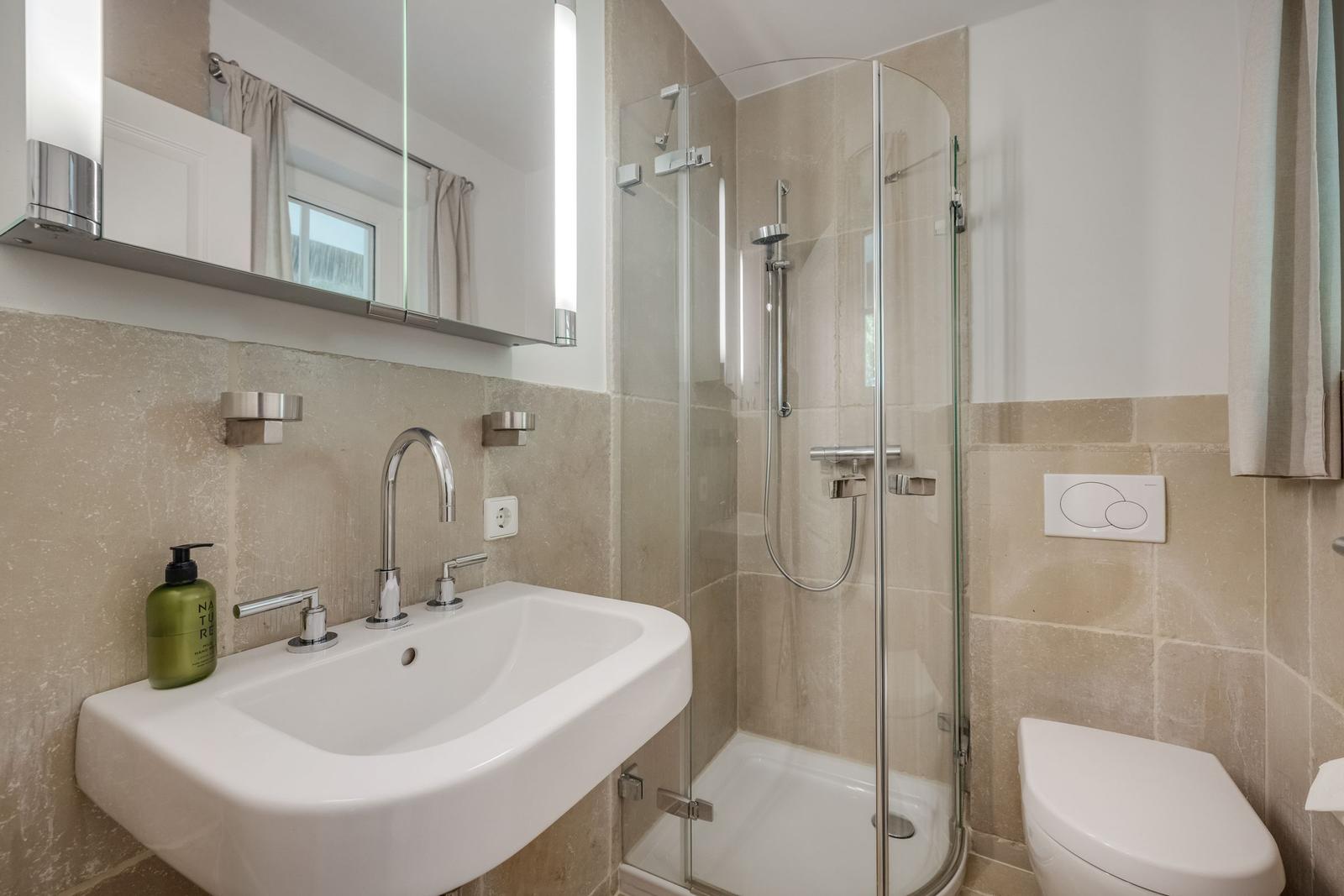 Bathroom with shower, sink, and toilet. Lit mirror cabinet.