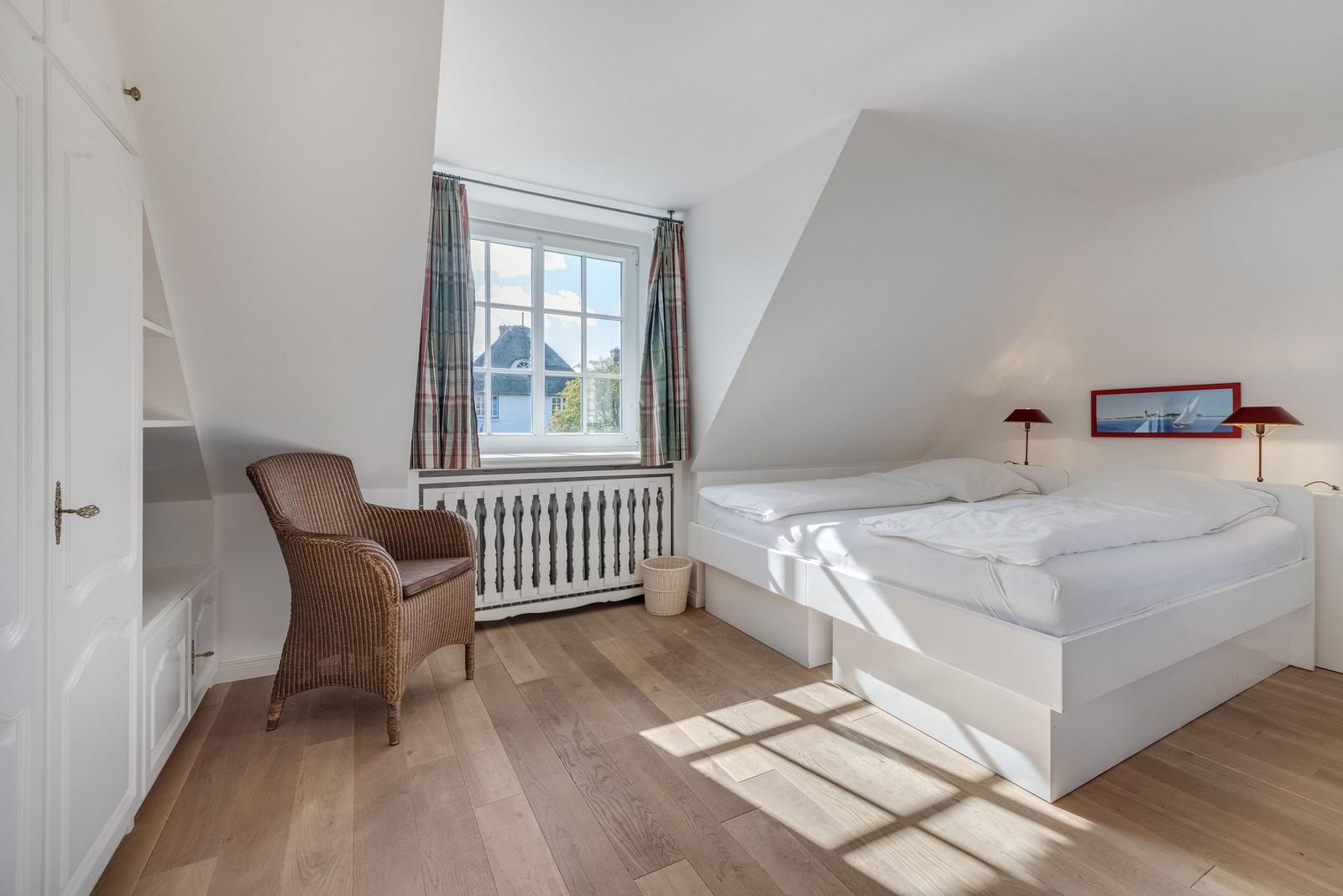 Bedroom with white bed, wooden floor, and window with curtains.