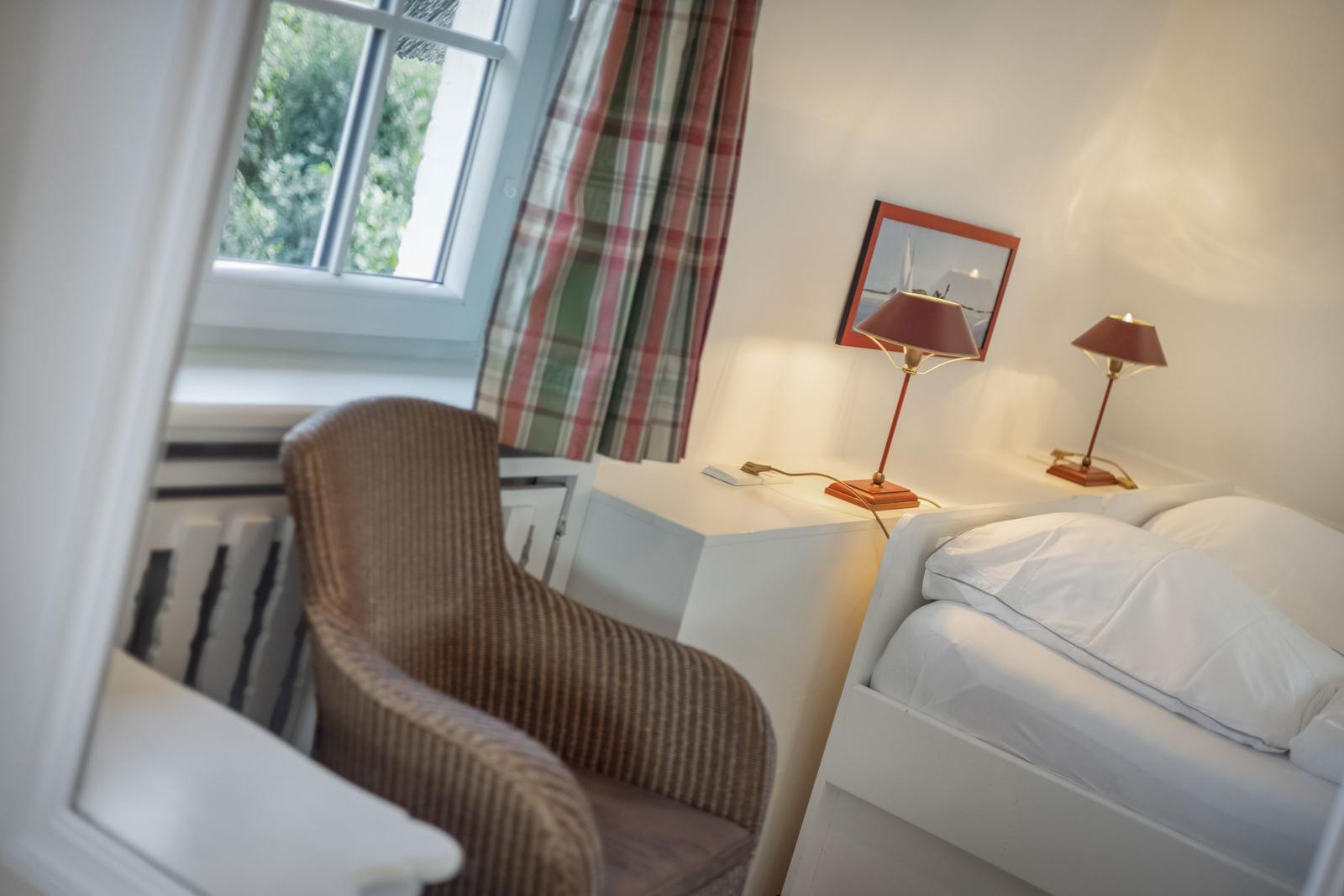 Bedroom with bed, nightstand, and chair. Window with curtains.