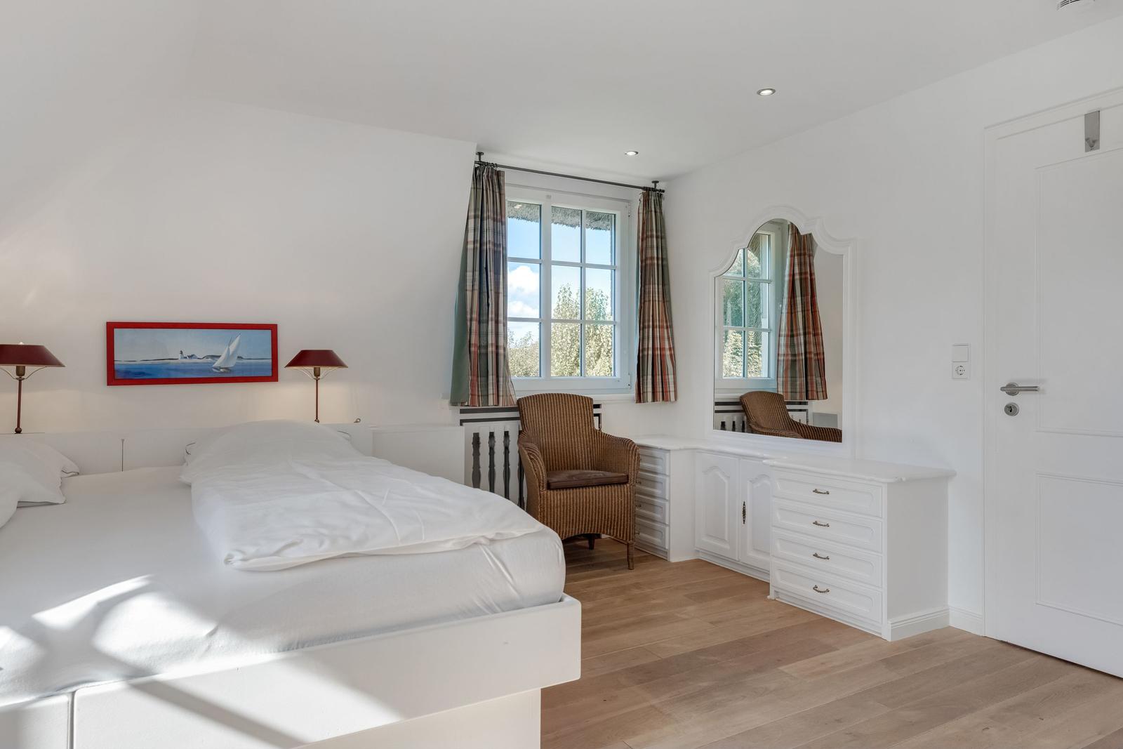 Bedroom with white bed, window, mirror and chair.