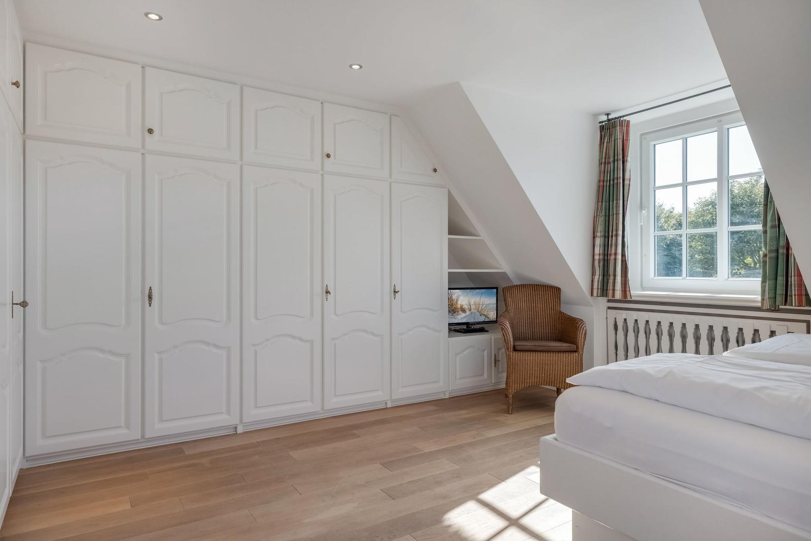 Bedroom with white closet, bed, chair, and window.