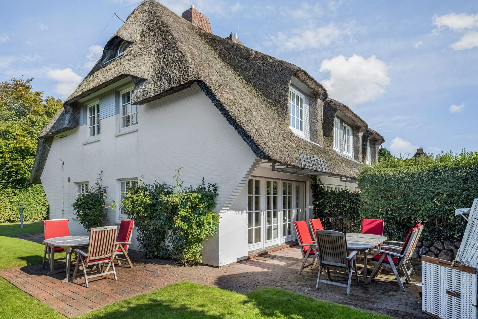 White villa with thatched roof and terrace with tables and chairs.