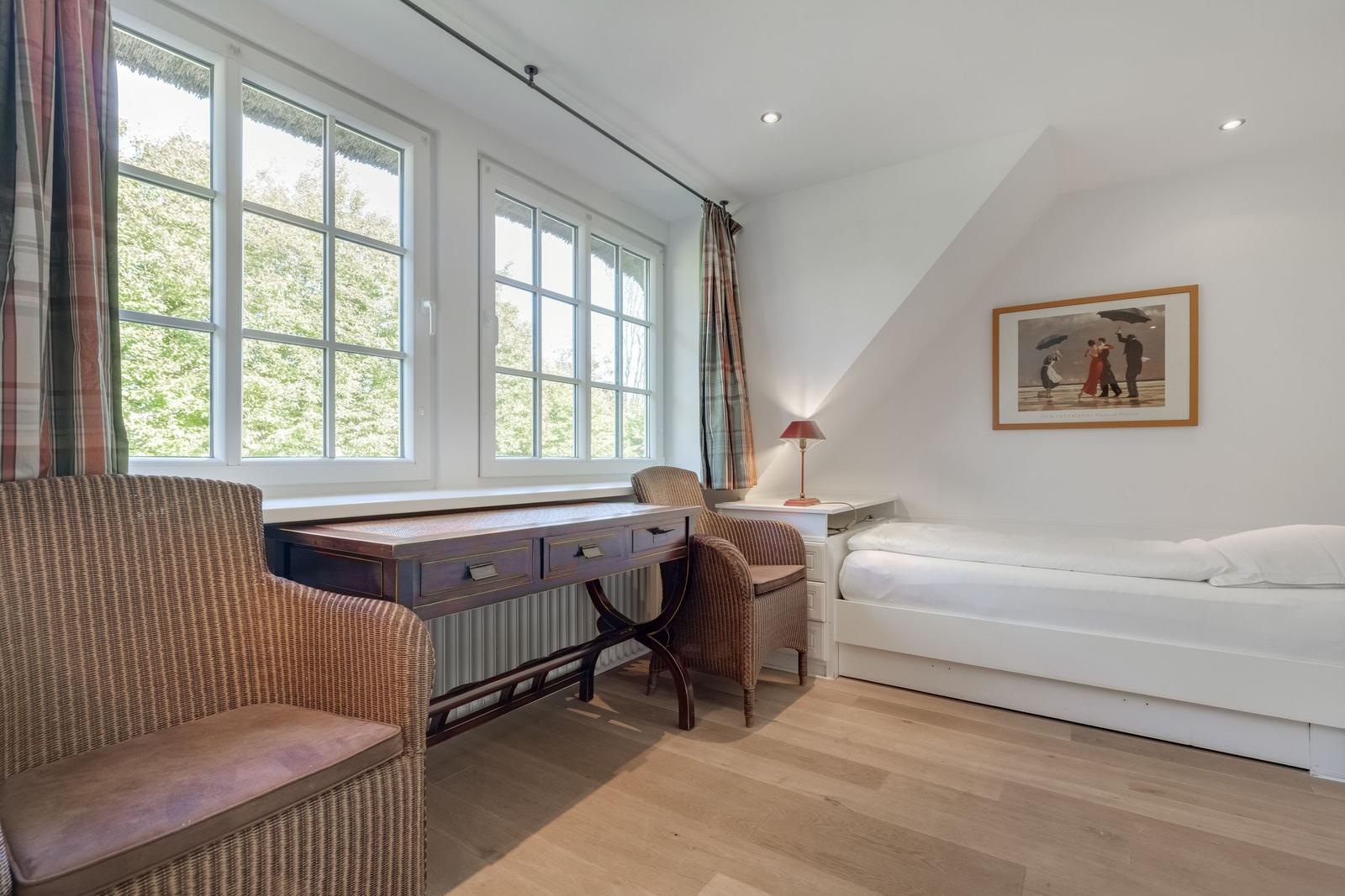 Room with desk, bed, and windows overlooking trees.