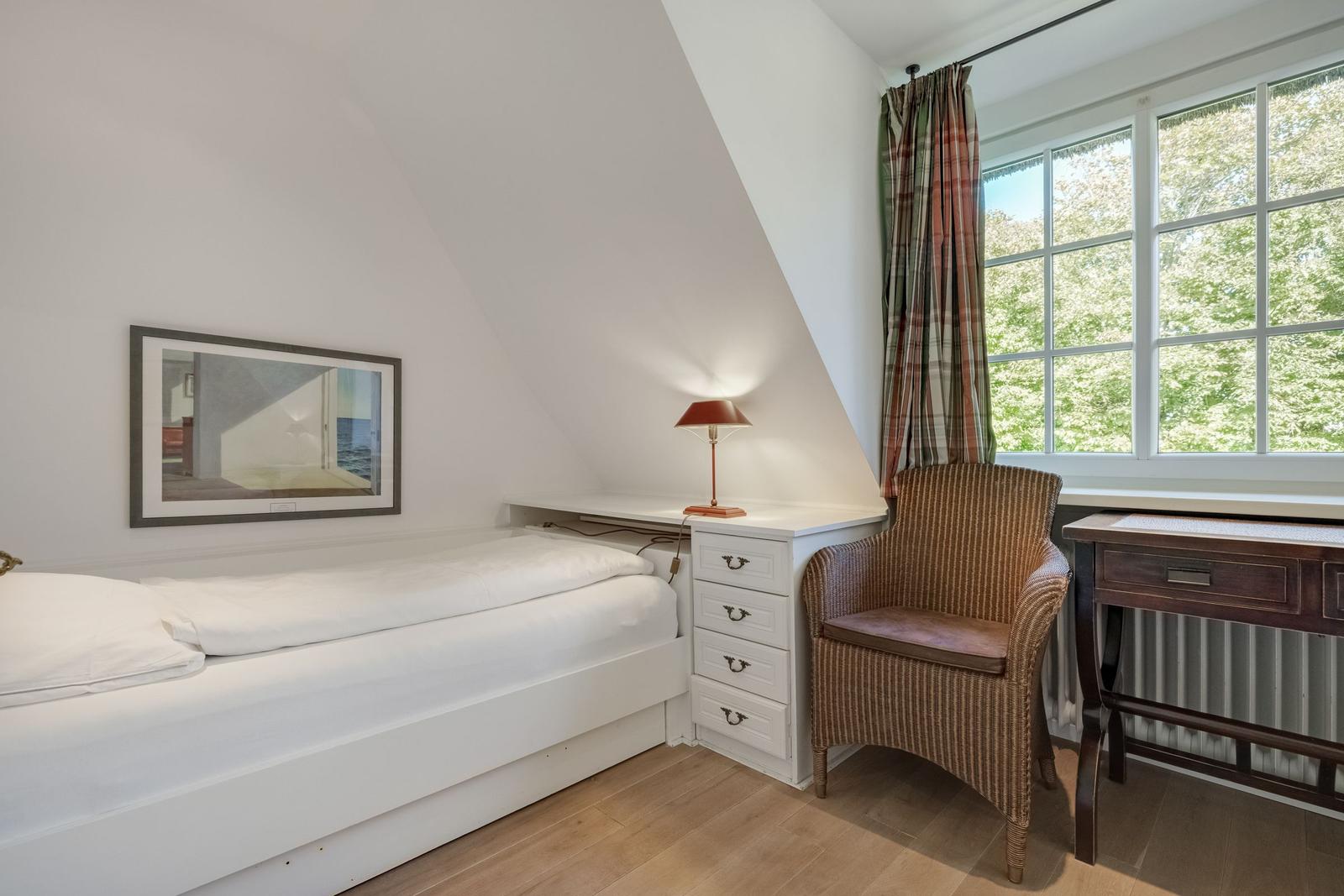 Bedroom with bed, desk, and chair. Window with curtain. Wall picture and nightstand.