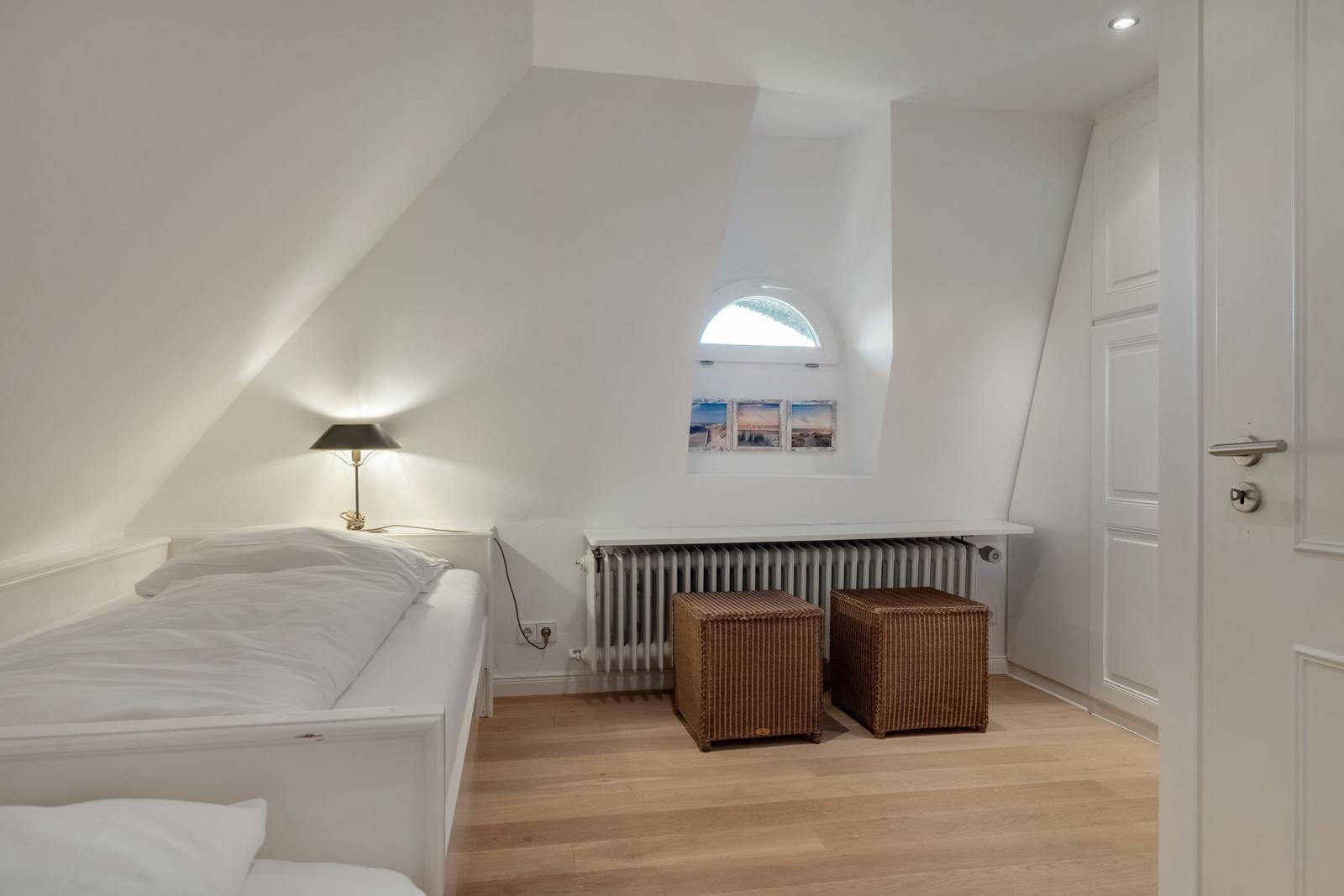 Bedroom with sloped ceiling, bed, lamp, window, and two baskets.
