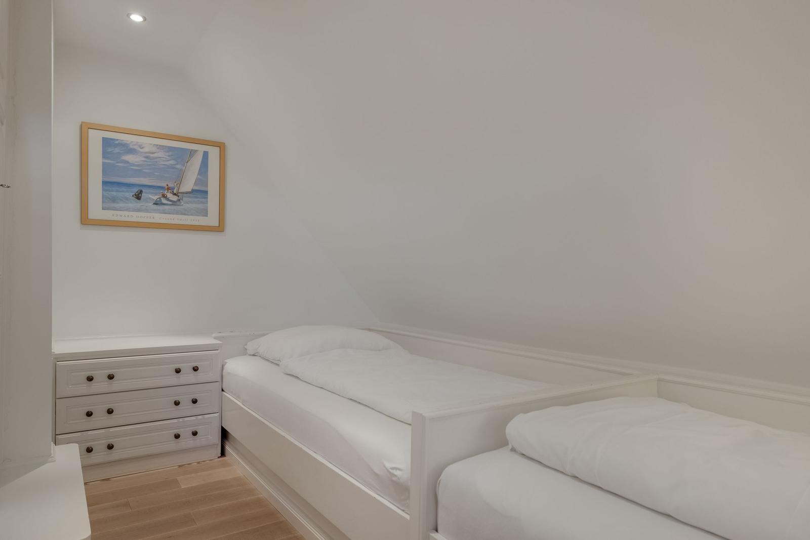 Room with two beds, dresser, and wall art on sloped ceiling.