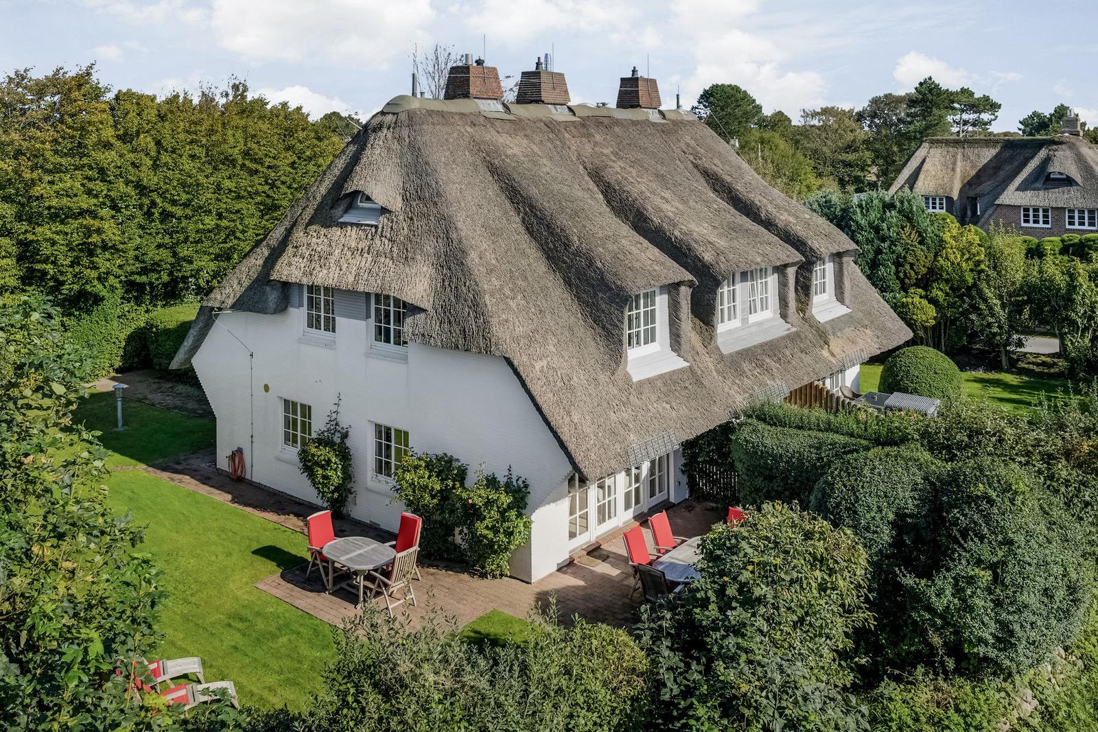 House with thatched roof, garden and red chairs