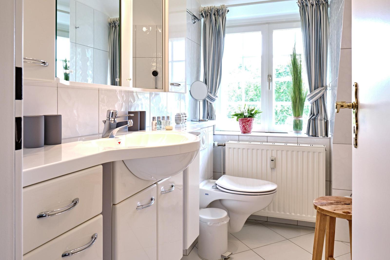 Badezimmer mit Waschbecken, Toilette und Fenster mit Vorhängen.