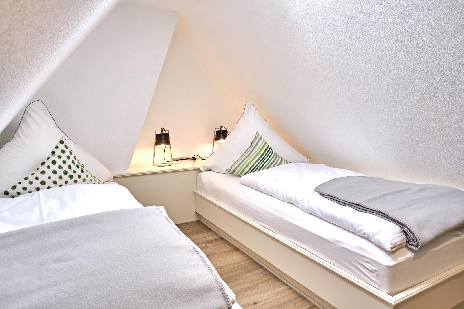 Zwei Einzelbetten unter Dachschrägen mit Nachttisch und Lampen.