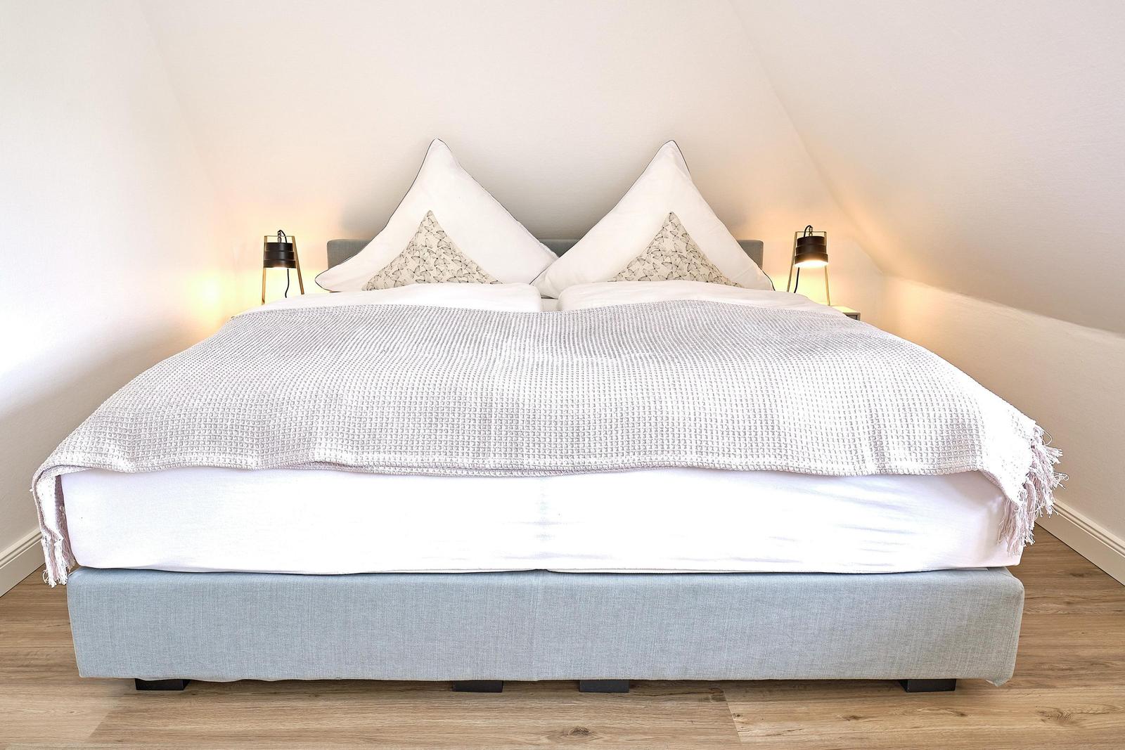 Doppelbett mit hellblauem Gestell und weißen Kissen unter schrägen Wänden.