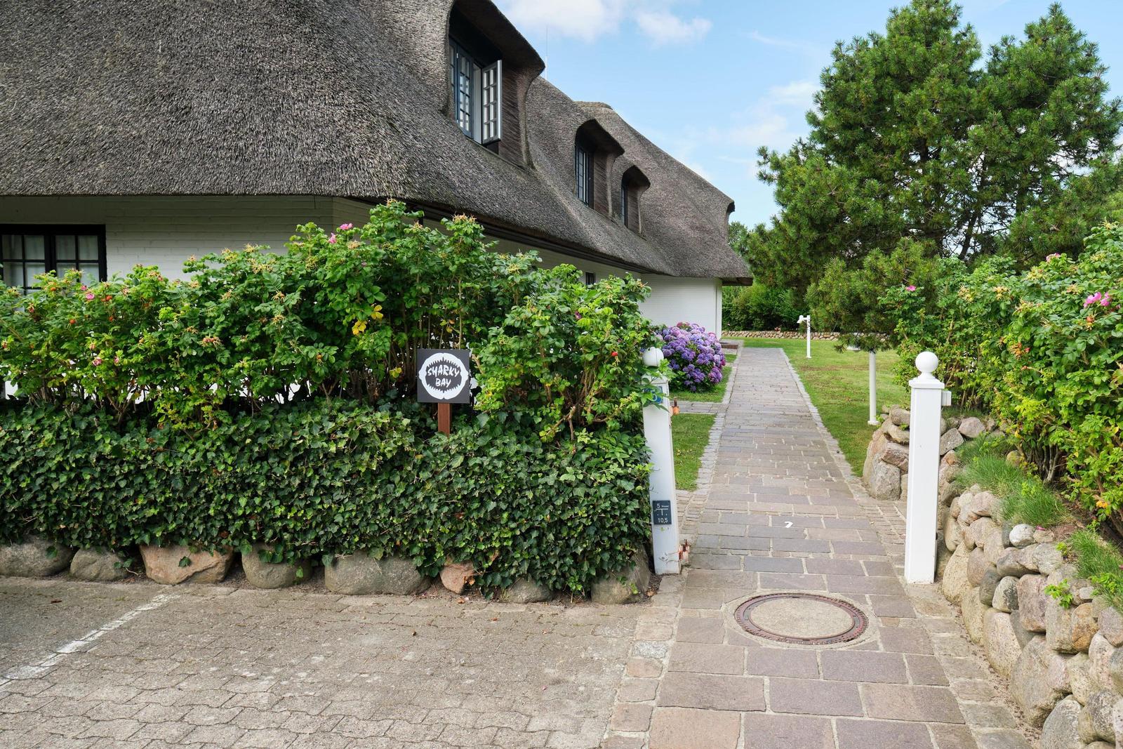 Steinweg führt zu einem Haus mit Strohdach und grüner Hecke.