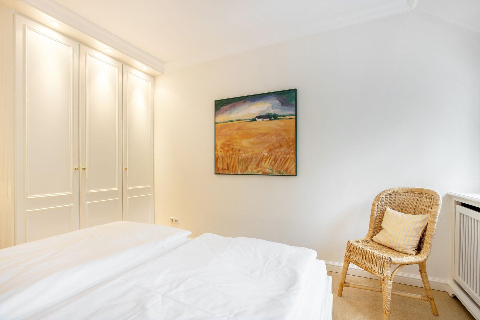 Bedroom with bed, wardrobe, and chair with cushion.