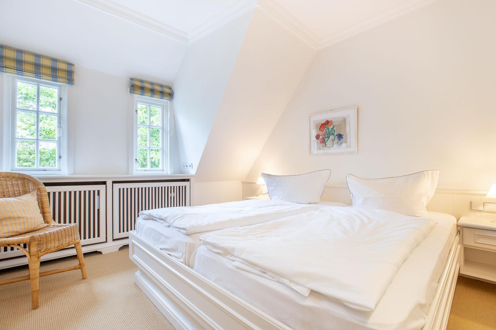 Bedroom with double bed, two windows, and a chair.