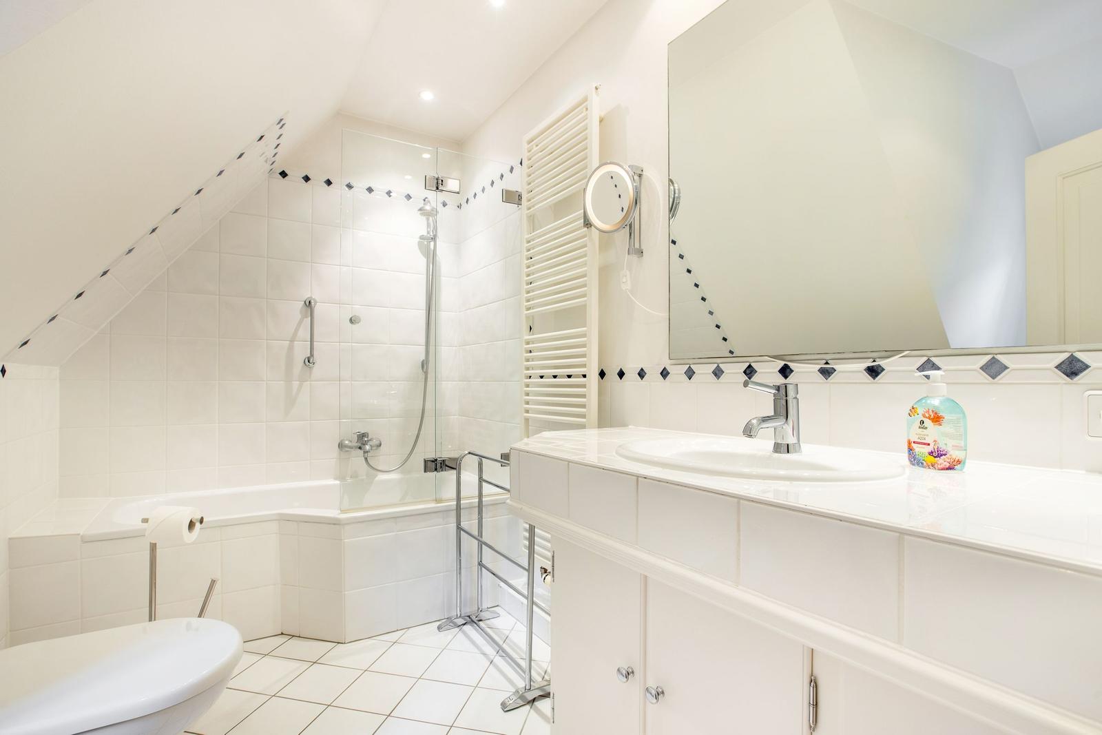 Bathroom with shower, sink, and toilet. White tiles and mirror.