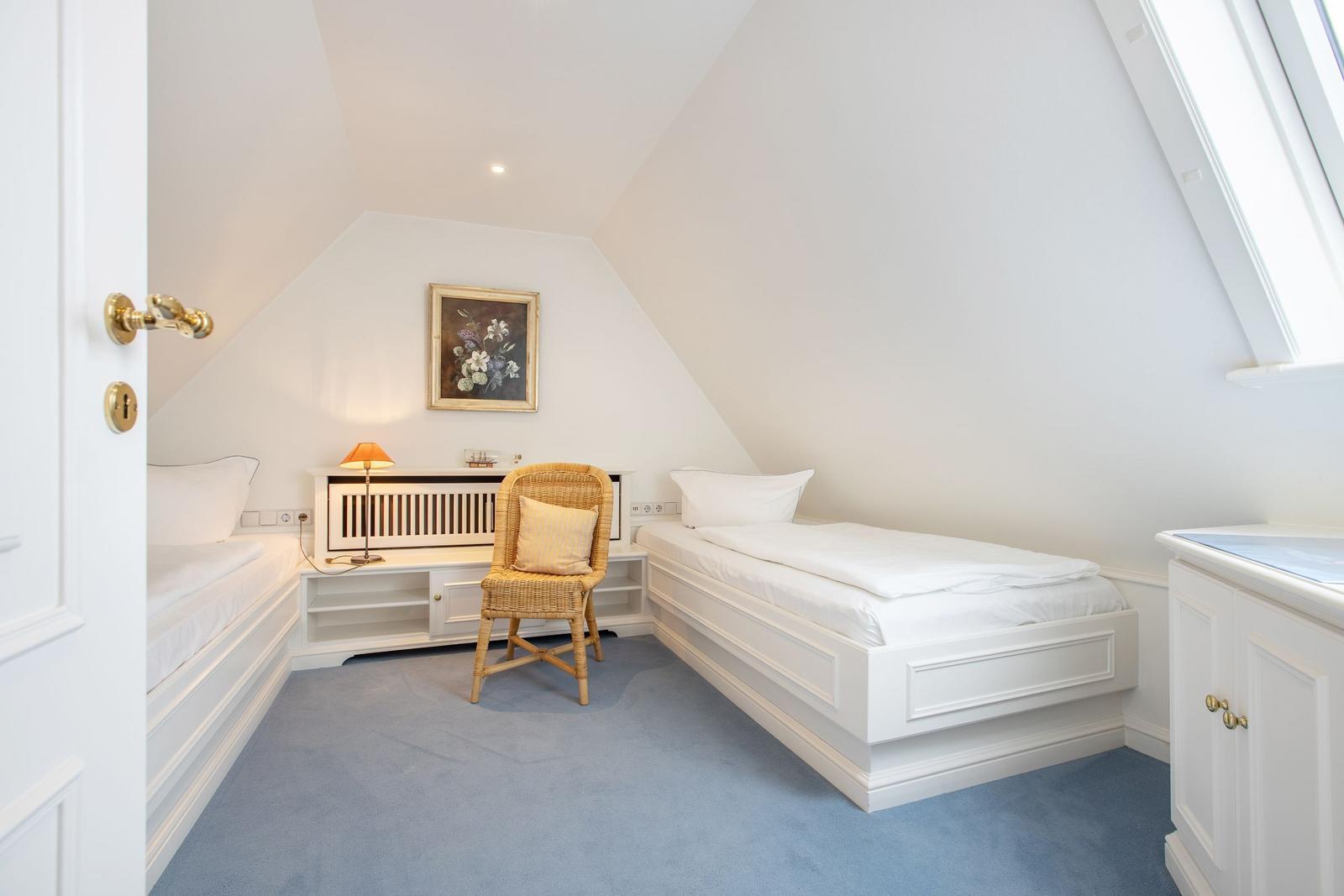 Room with two beds, chair, and window. Wall picture and lamp visible.