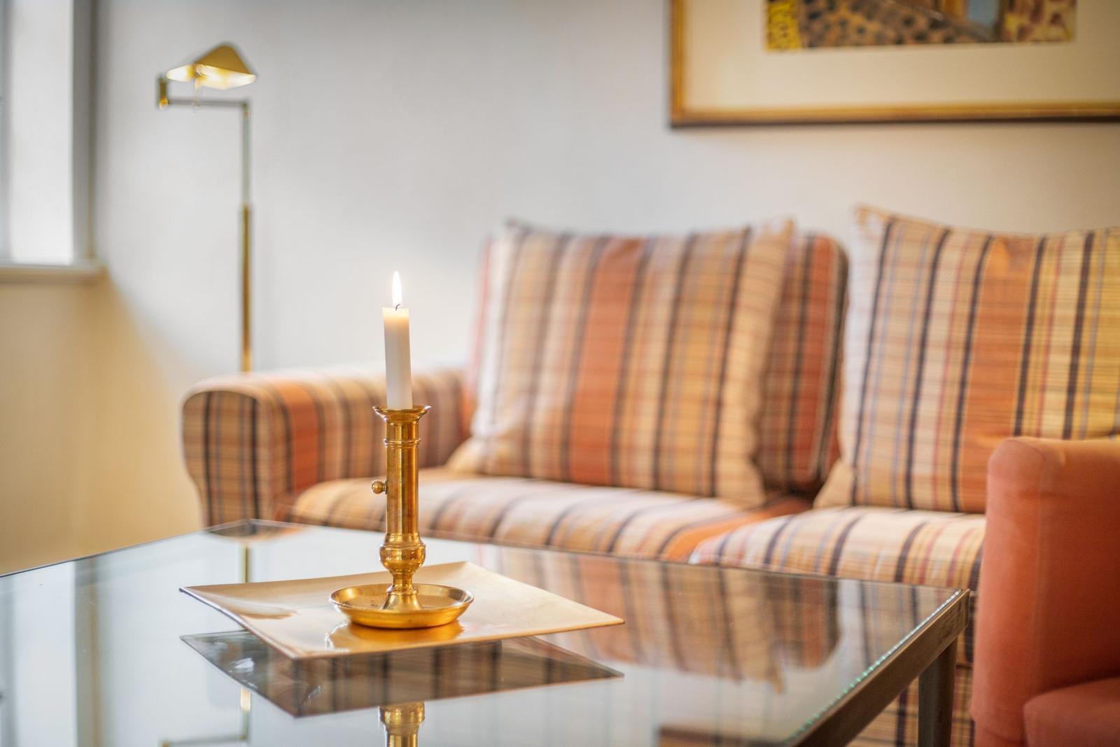 A glass table with a candle and brass holder in front of a sofa with checkered upholstery.