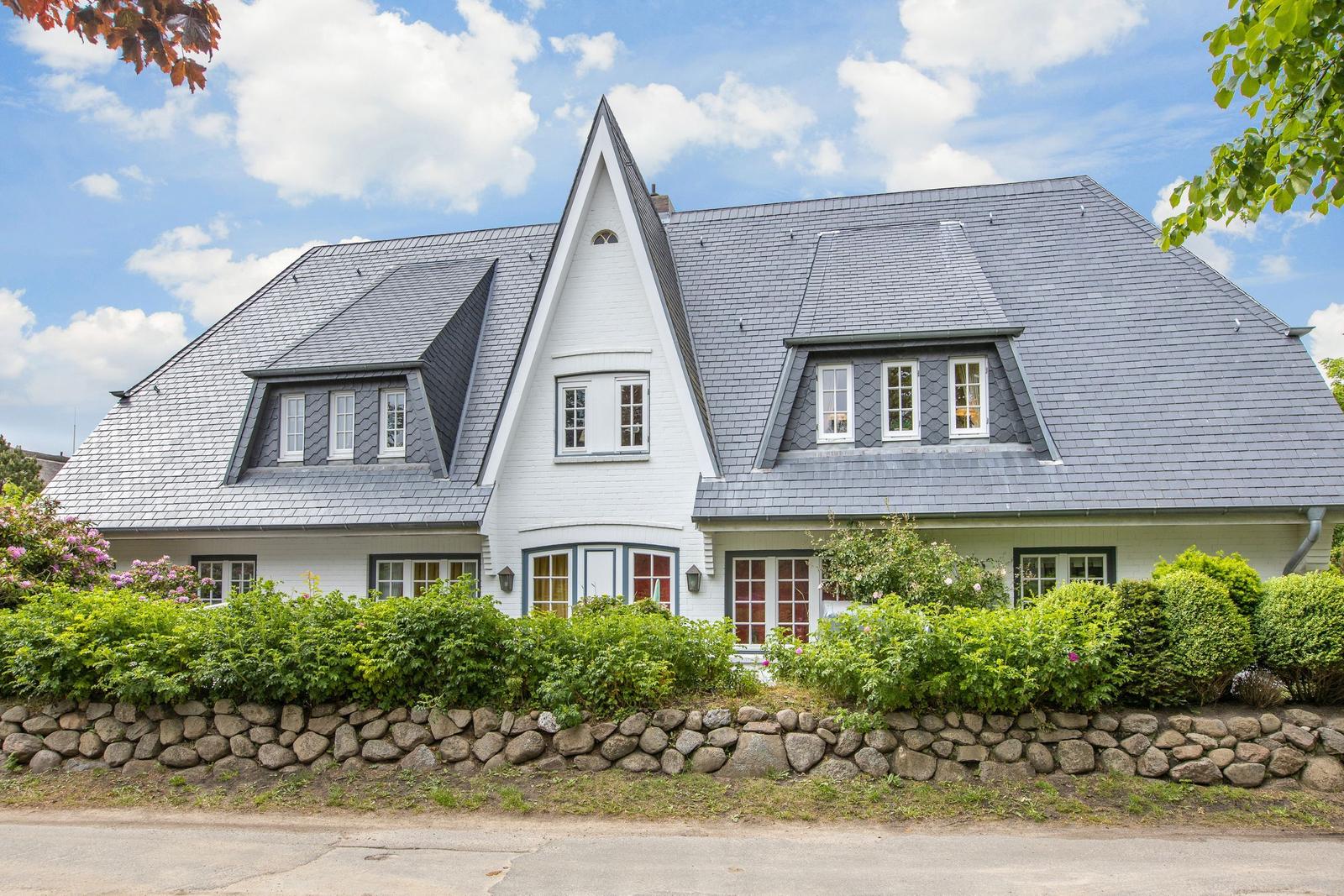 A white house with a gray roof and green surroundings.