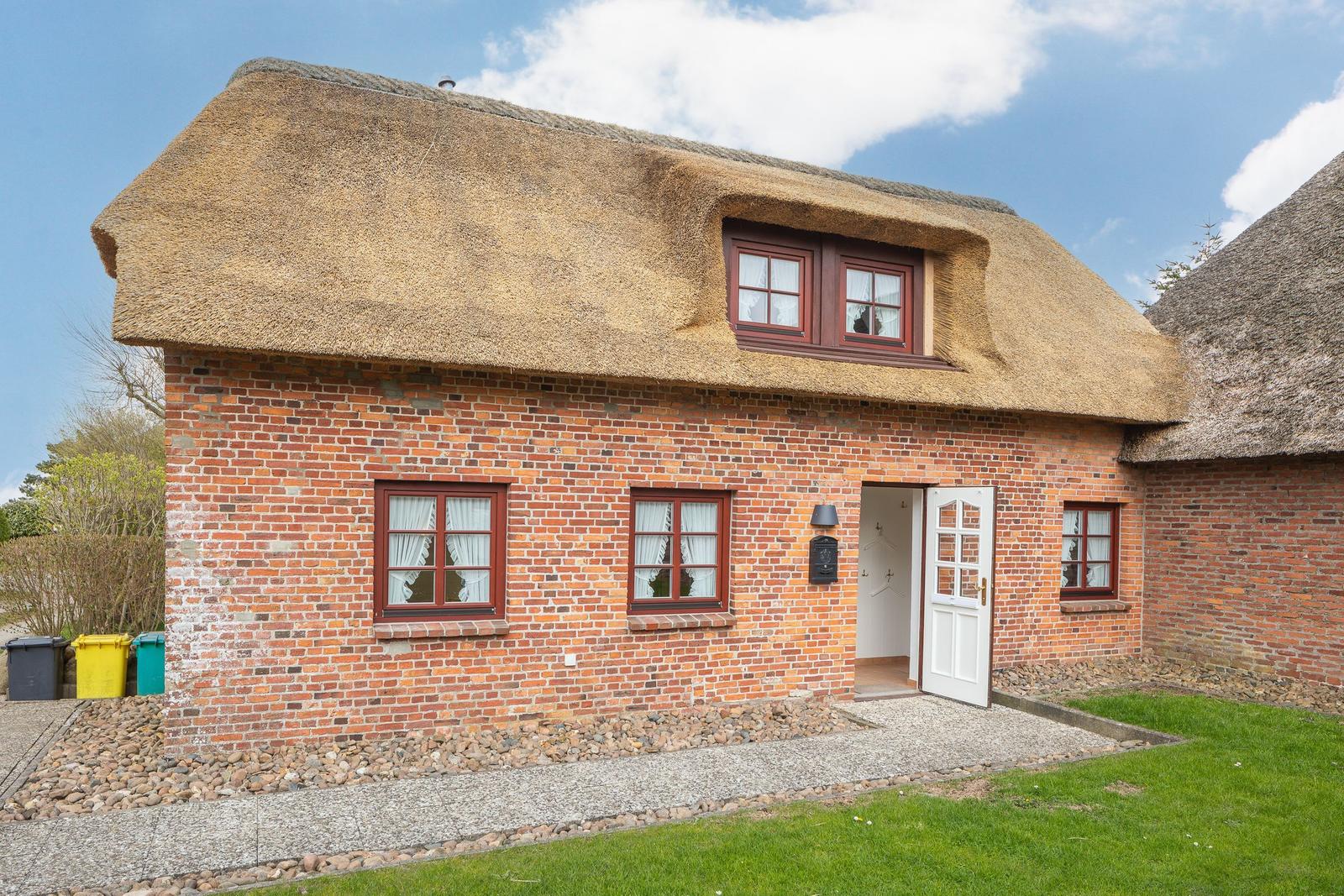 Haus mit strohgedecktem Dach und rotem Backsteinmauerwerk. Weiße Tür und Fenster mit weißen Vorhängen.