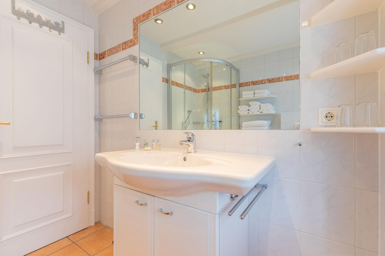 Badezimmer mit Waschbecken, Spiegel und Dusche.