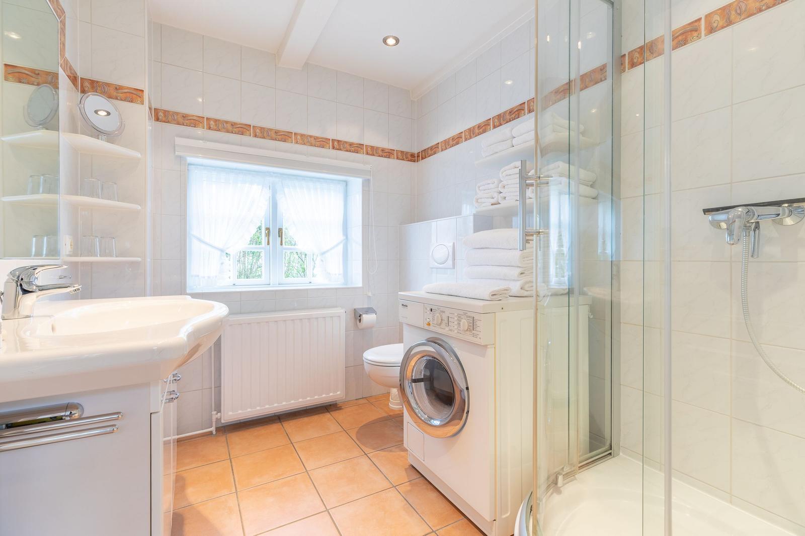 Badezimmer mit Dusche, Waschmaschine und Fenster.