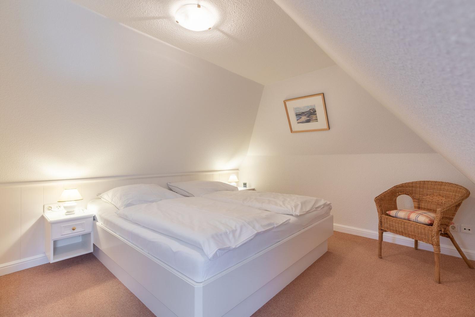 Schlafzimmer mit Doppelbett, Nachttisch und Stuhl unter schrägen Wänden.