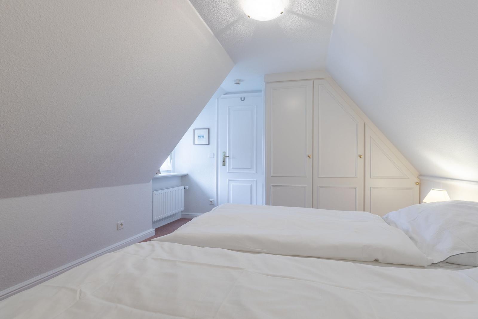 Schlafzimmer mit Dachschrägen, weißem Bett und Kleiderschrank.