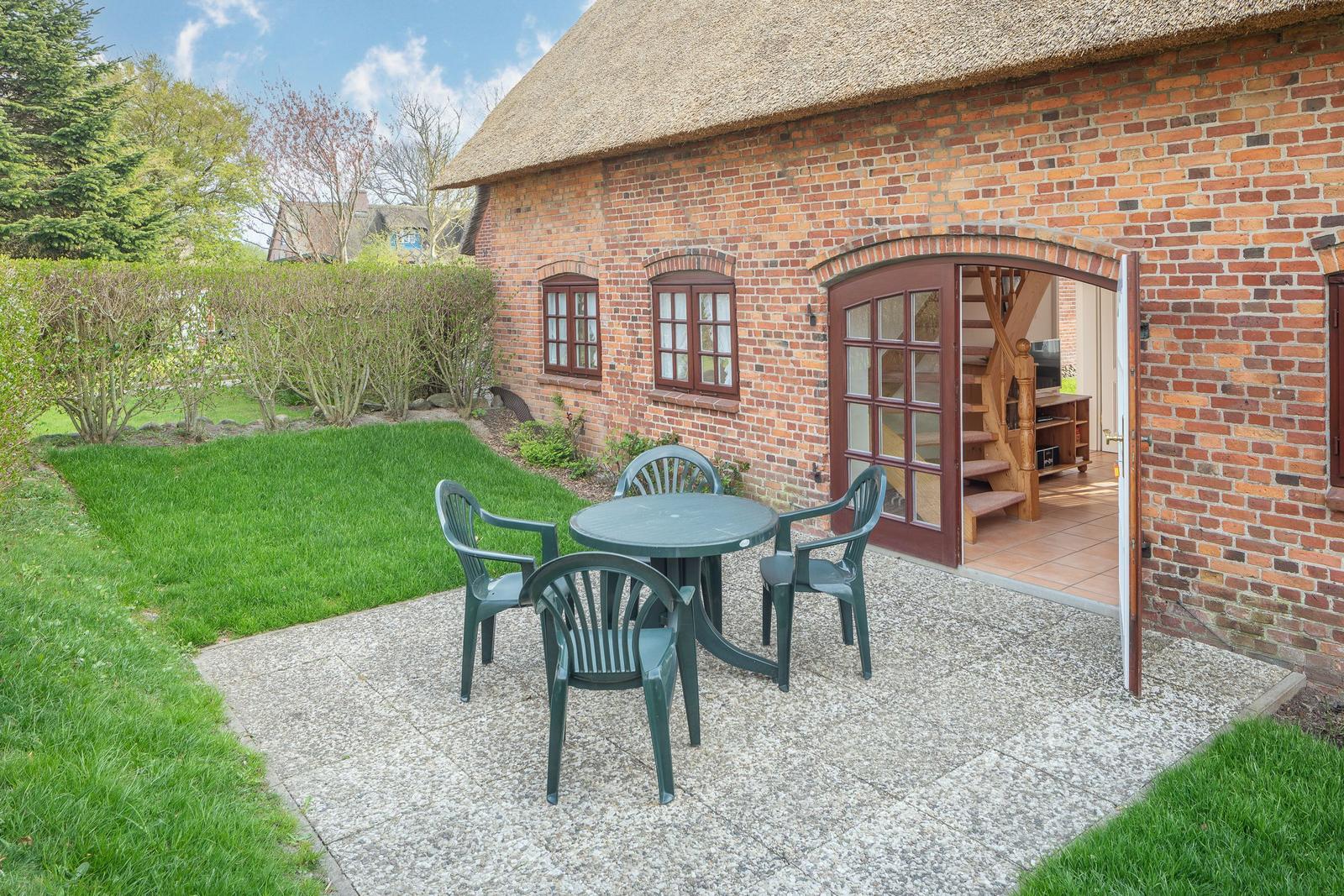 Roter Backsteinbau mit strohgedecktem Dach und Gartenbereich mit Tisch und Stühlen.