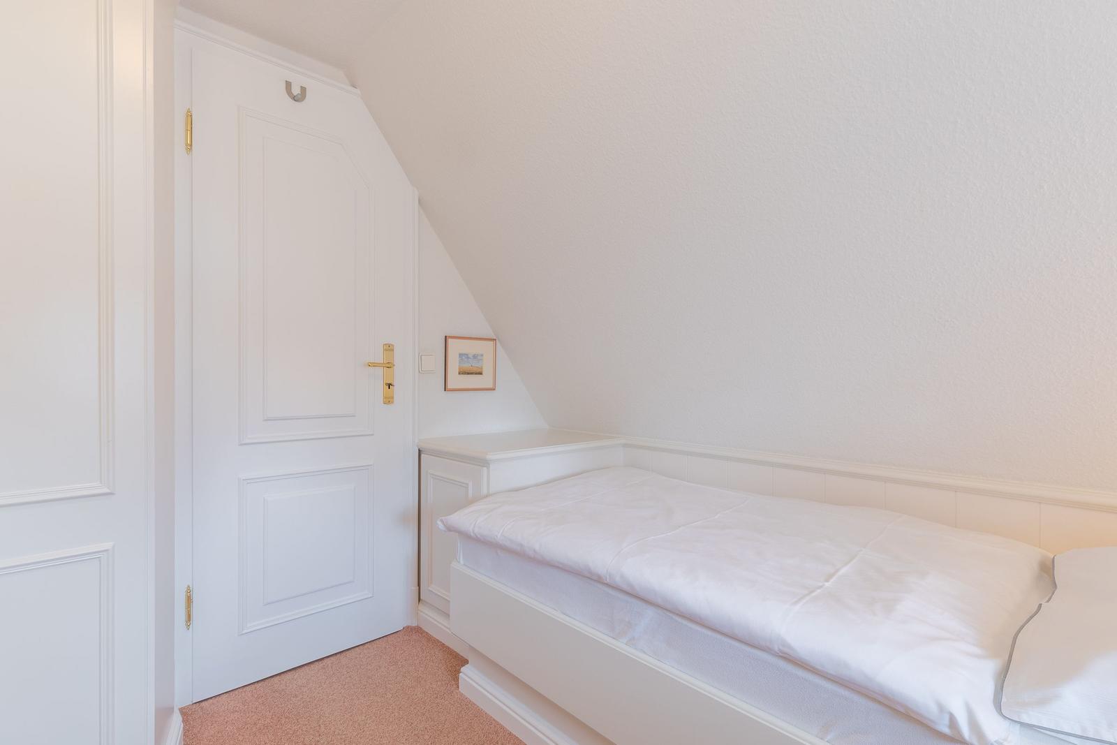 Ein Schlafzimmer mit weißem Bett und Tür unter Dachschrägen.