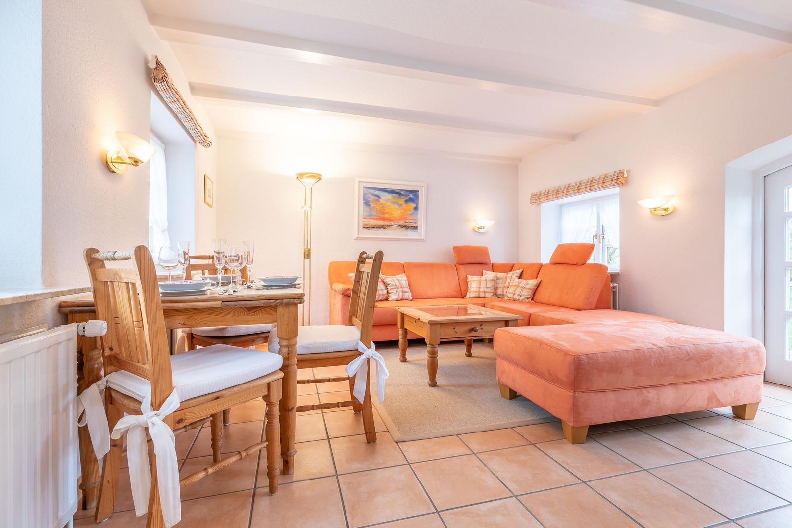 Wohn- und Essbereich mit orangefarbenem Sofa, Holztisch und Stühlen mit weißen Sitzkissen.