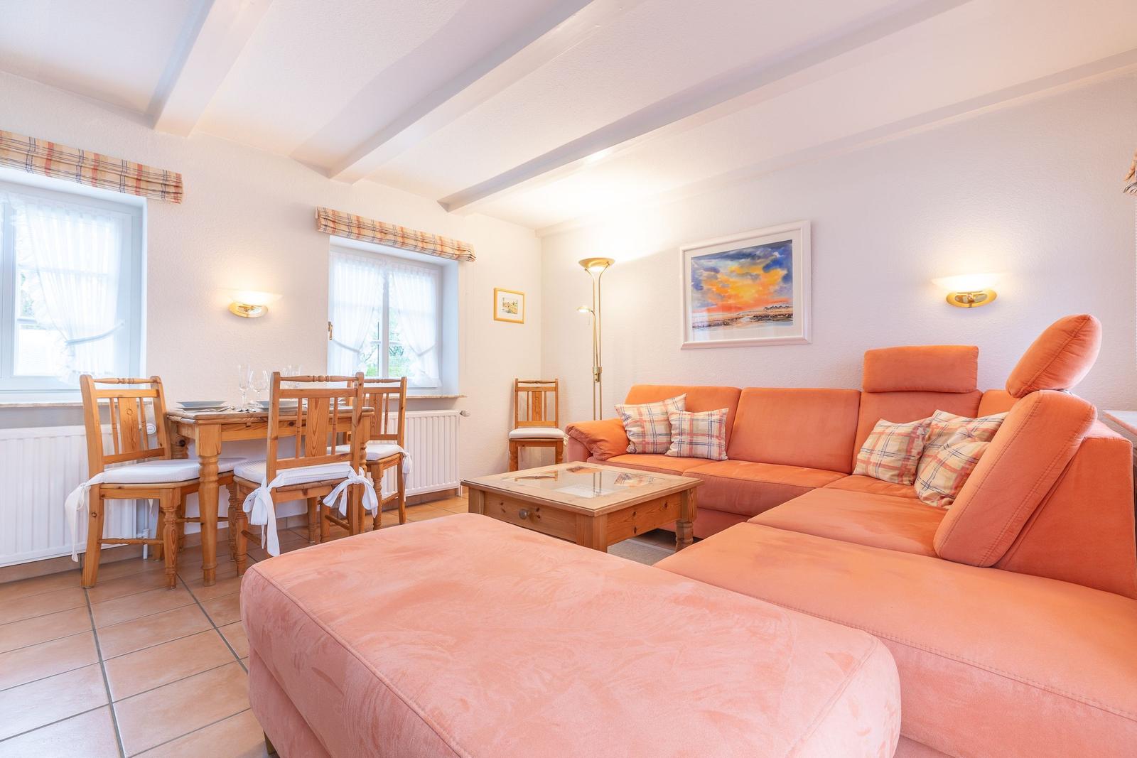 Wohn- und Essbereich mit orangefarbenem Sofa, Holztisch und Fenstern.
