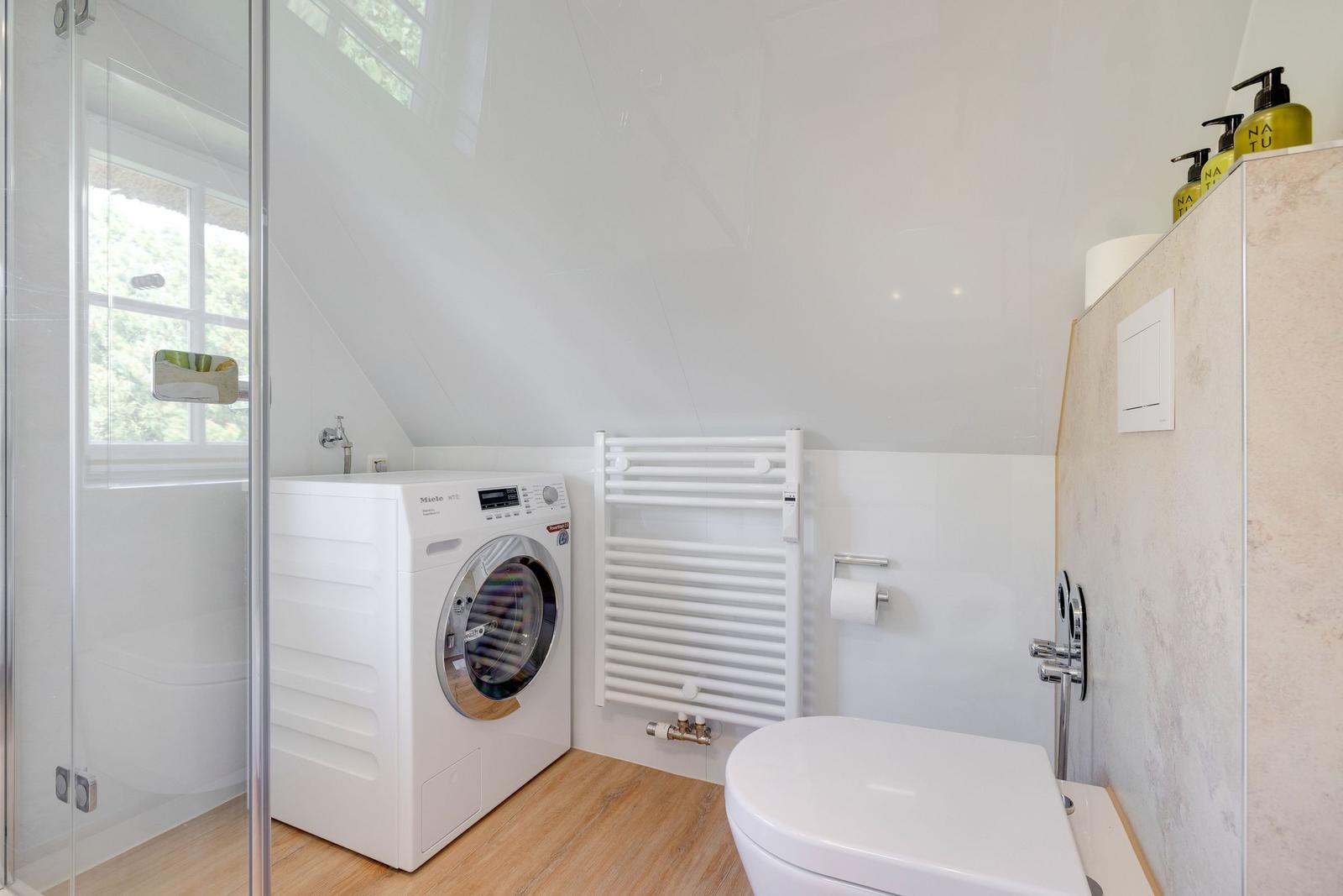 Badezimmer mit Waschmaschine, Toilette und Dusche unter Dach