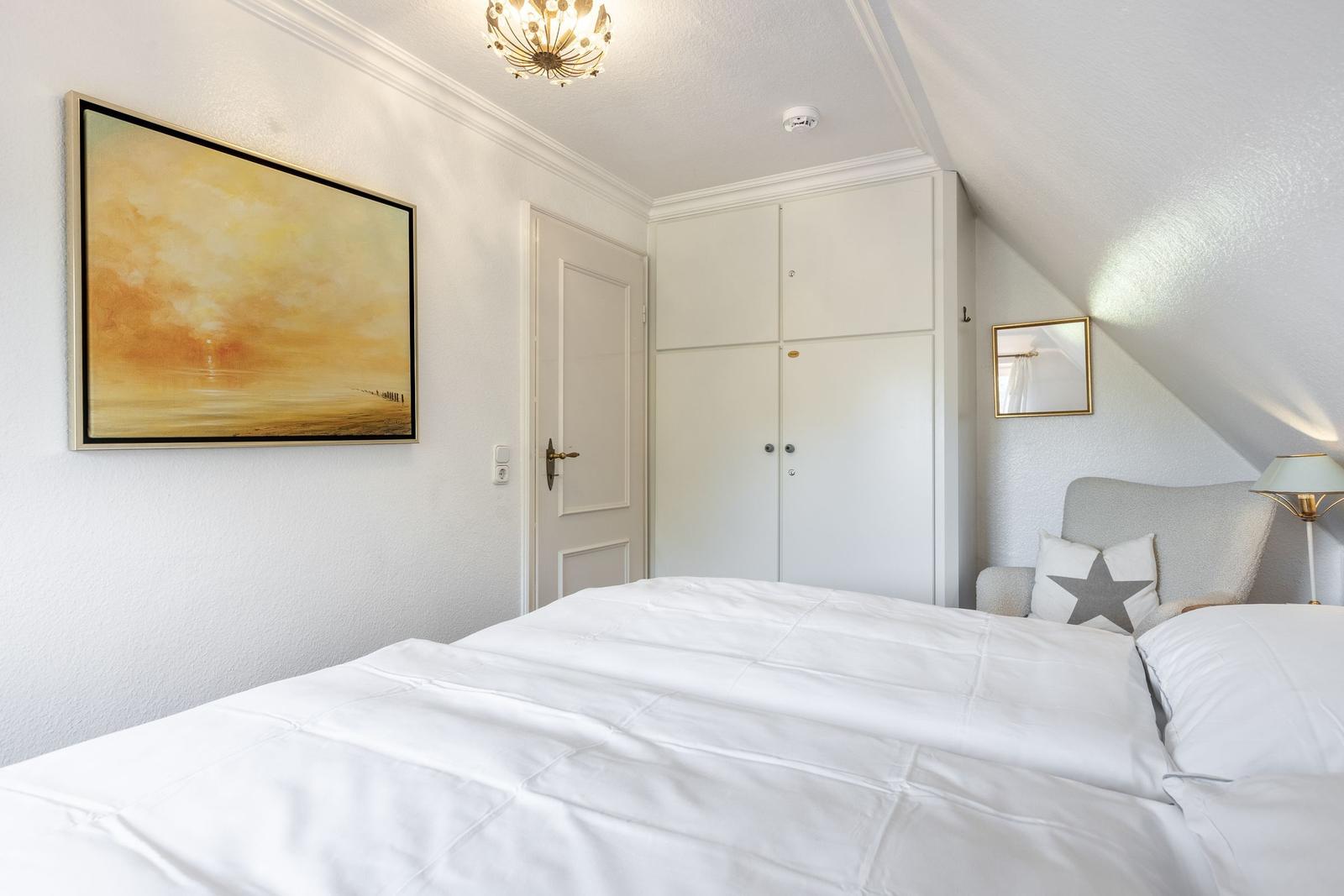 Schlafzimmer mit weißem Bett, Kleiderschrank und Wandbild.