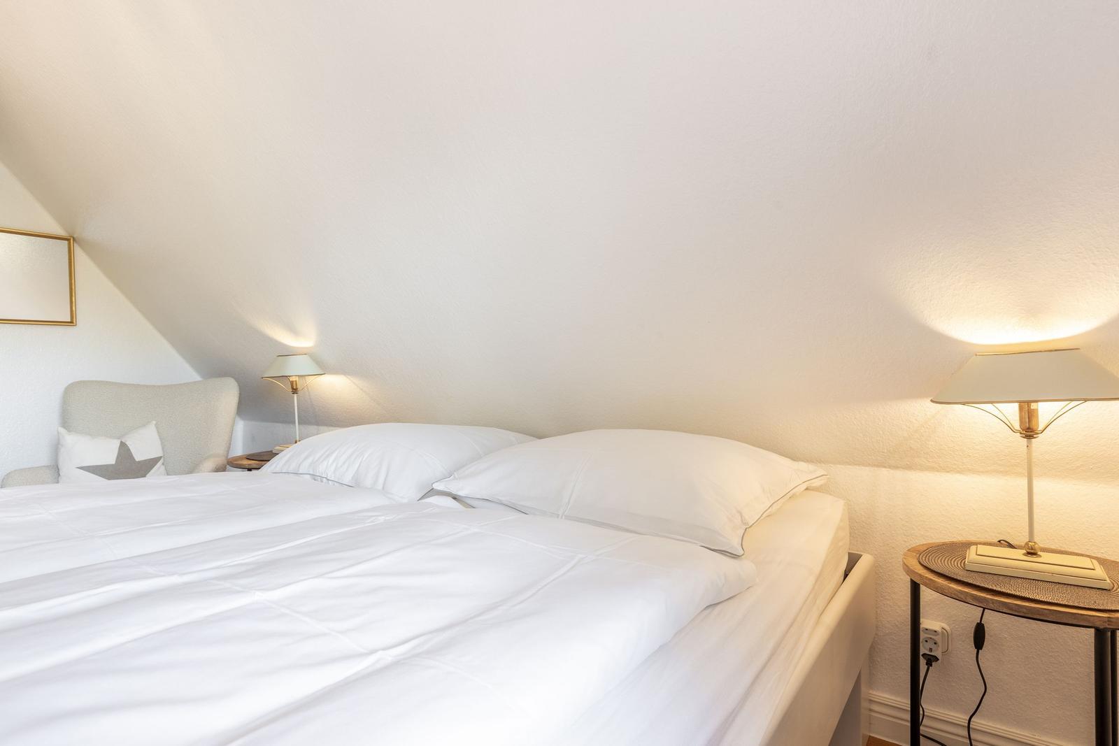 Schlafzimmer mit Doppelbett, zwei Nachttischen und Lampen an der schrägen Wand.