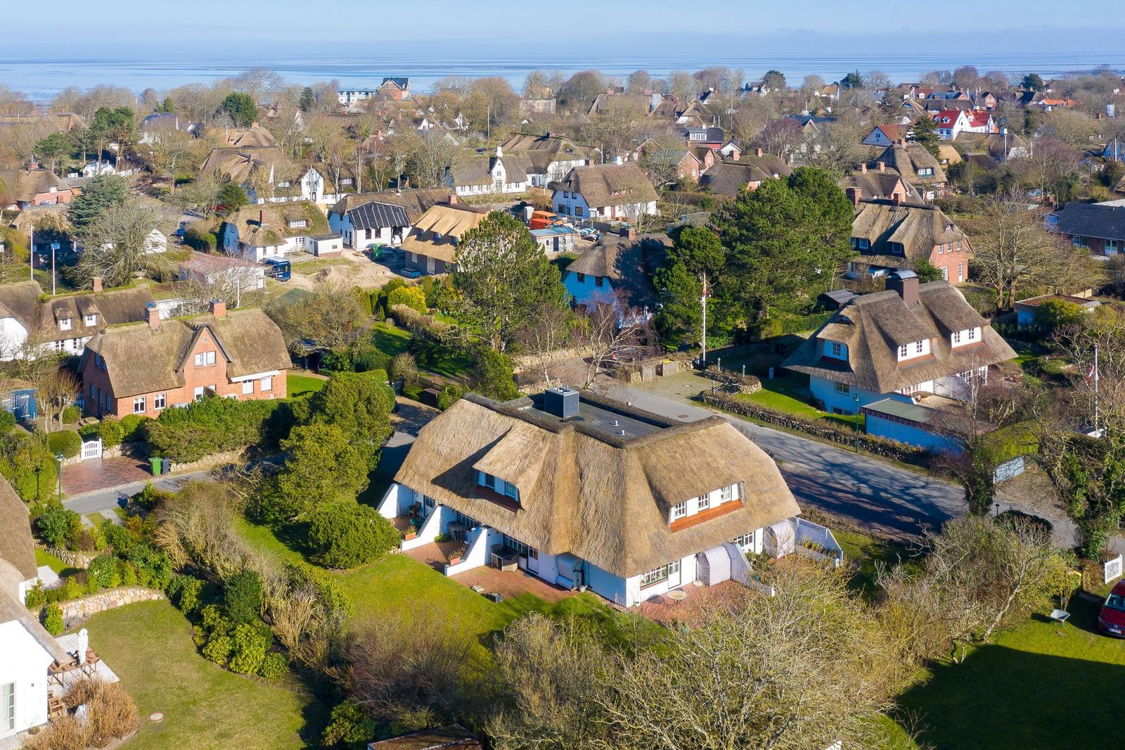Dorf mit strohgedeckten Häusern und grünen Gärten am Wasser