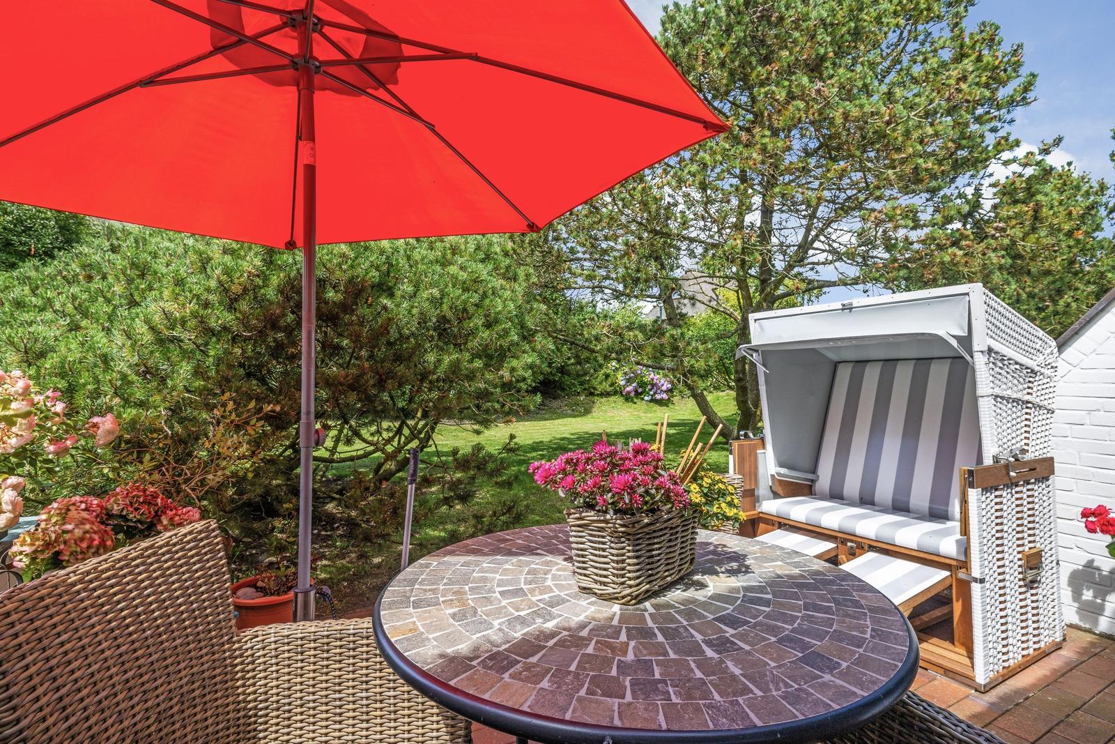 Terrasse mit rotem Sonnenschirm, runden Tisch und Strandkorb.