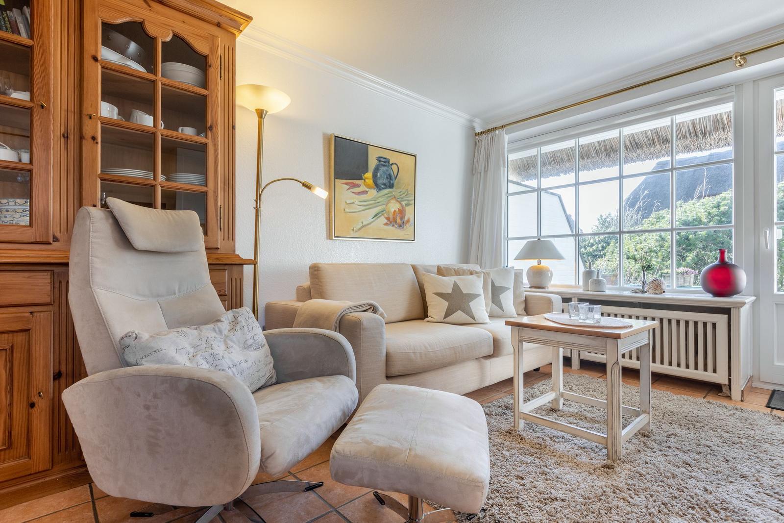Wohnzimmer mit Sofa, Sessel und Holzschrank. Fenster mit Blick auf Dächer.