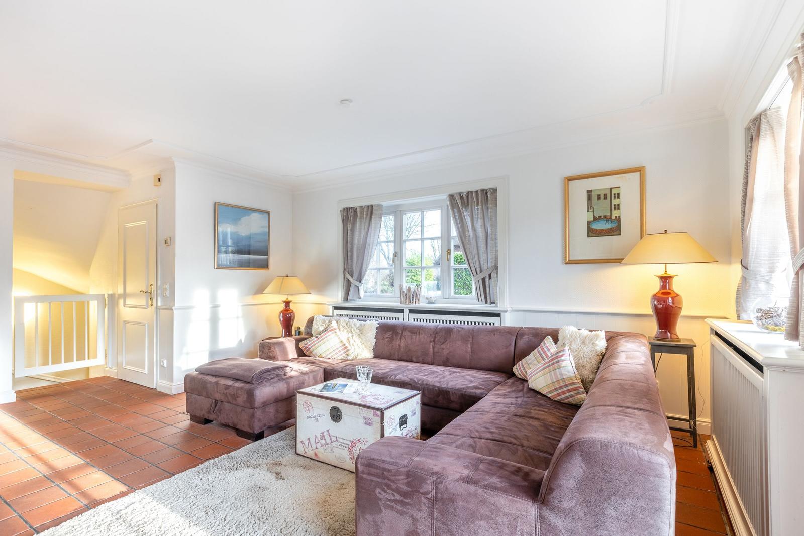 Living room with L-shaped sofa, cushions, and table. Windows with curtains and wall art.