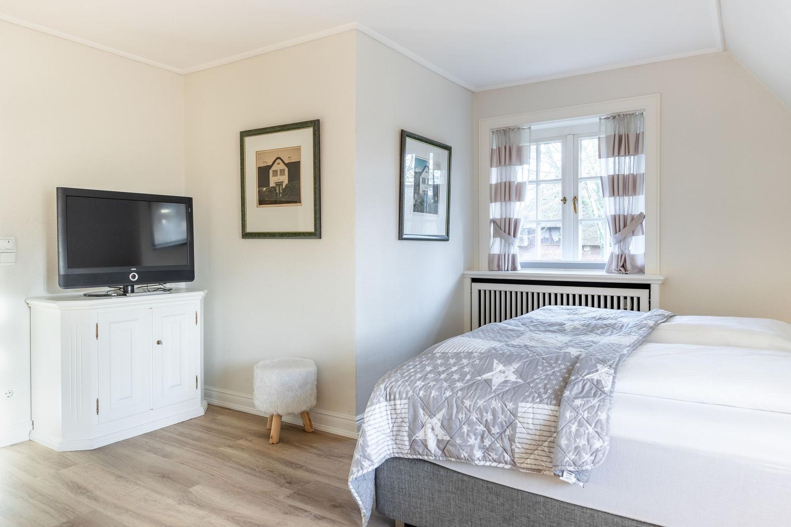 Bedroom with bed, TV, and window with curtains.