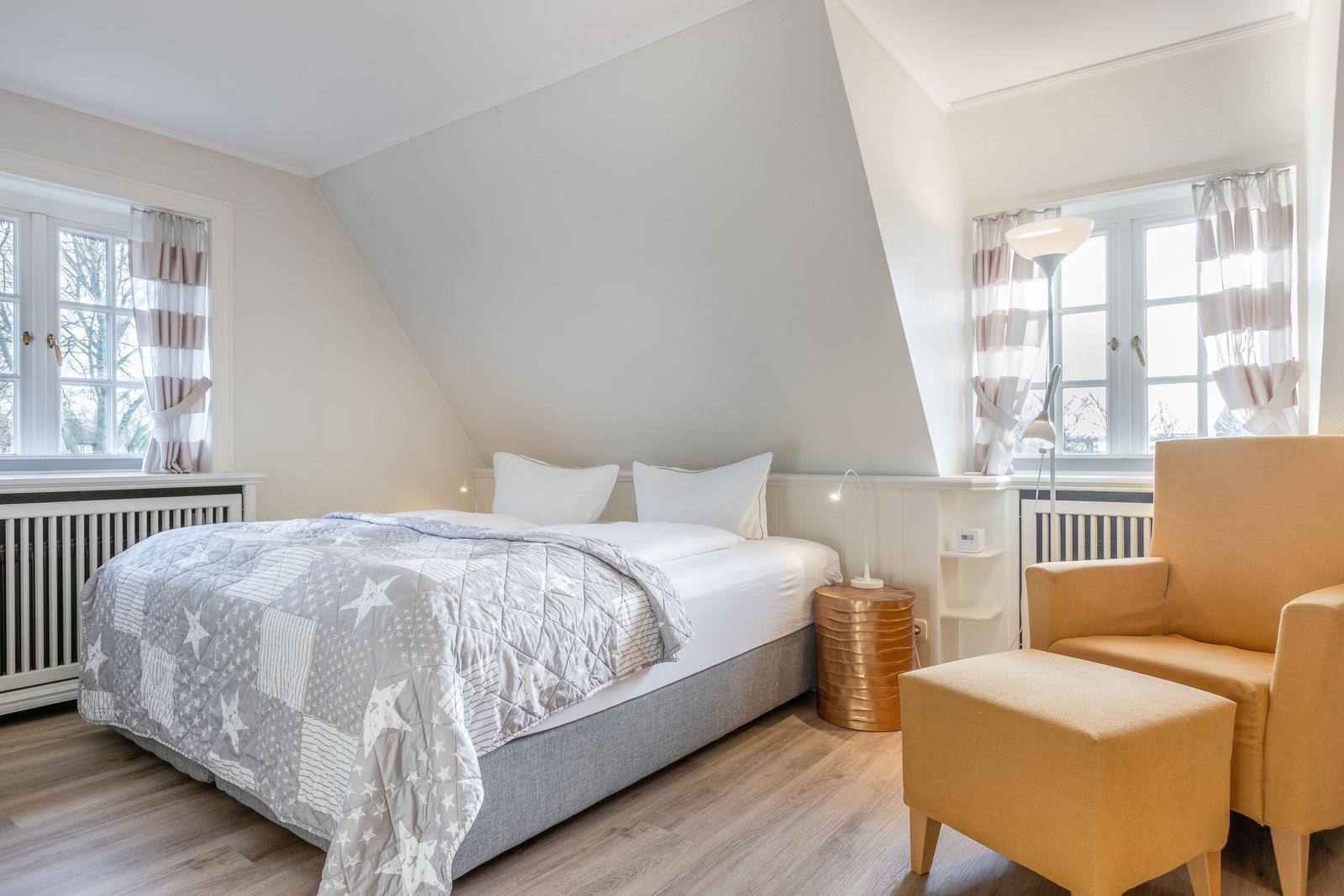 Bedroom with bed, armchair, and two windows.