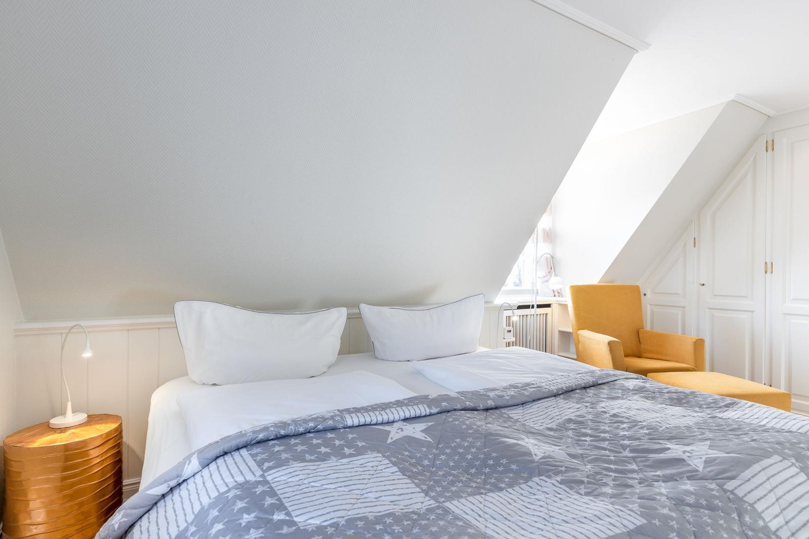 Bedroom with sloped ceiling, bed with gray coverlet, and yellow seating area.